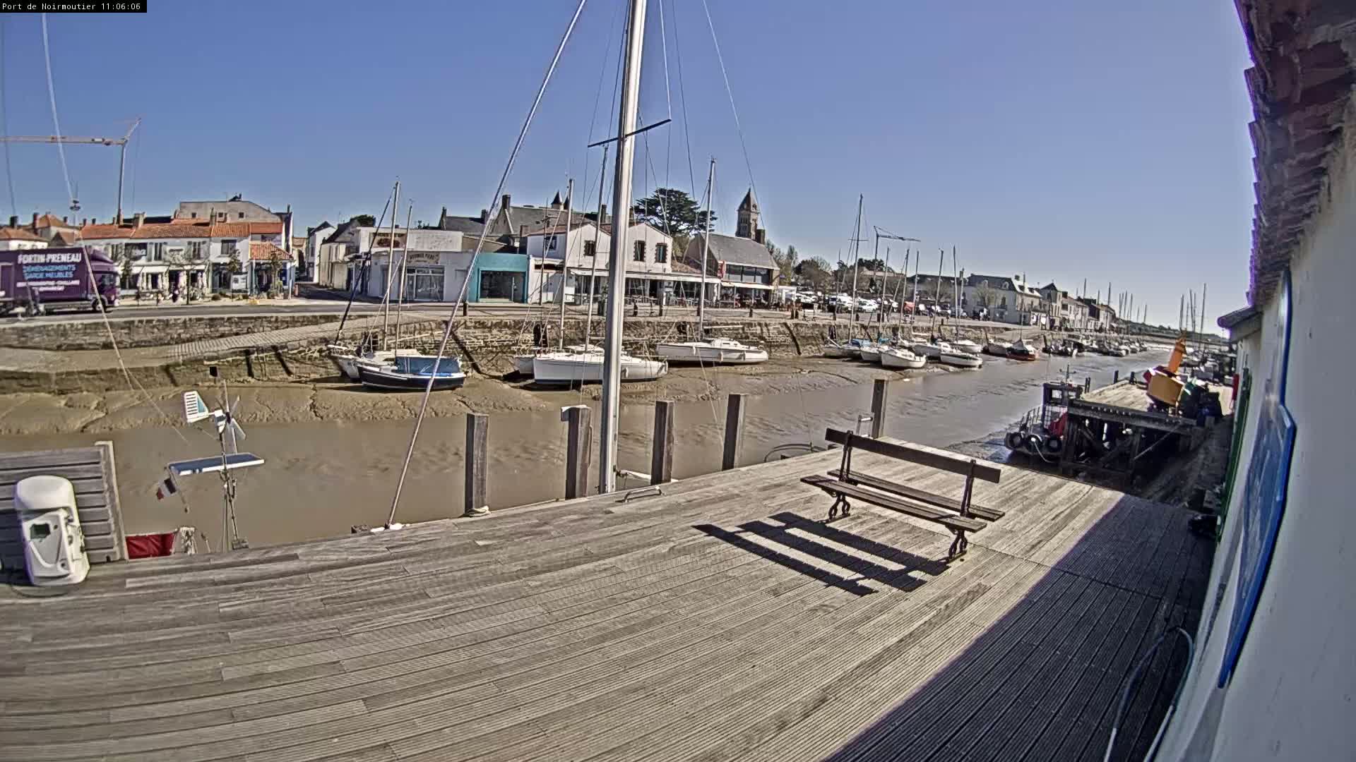 A wooden dock overlooks a harbor with sailboats at low tide under a clear blue sky.