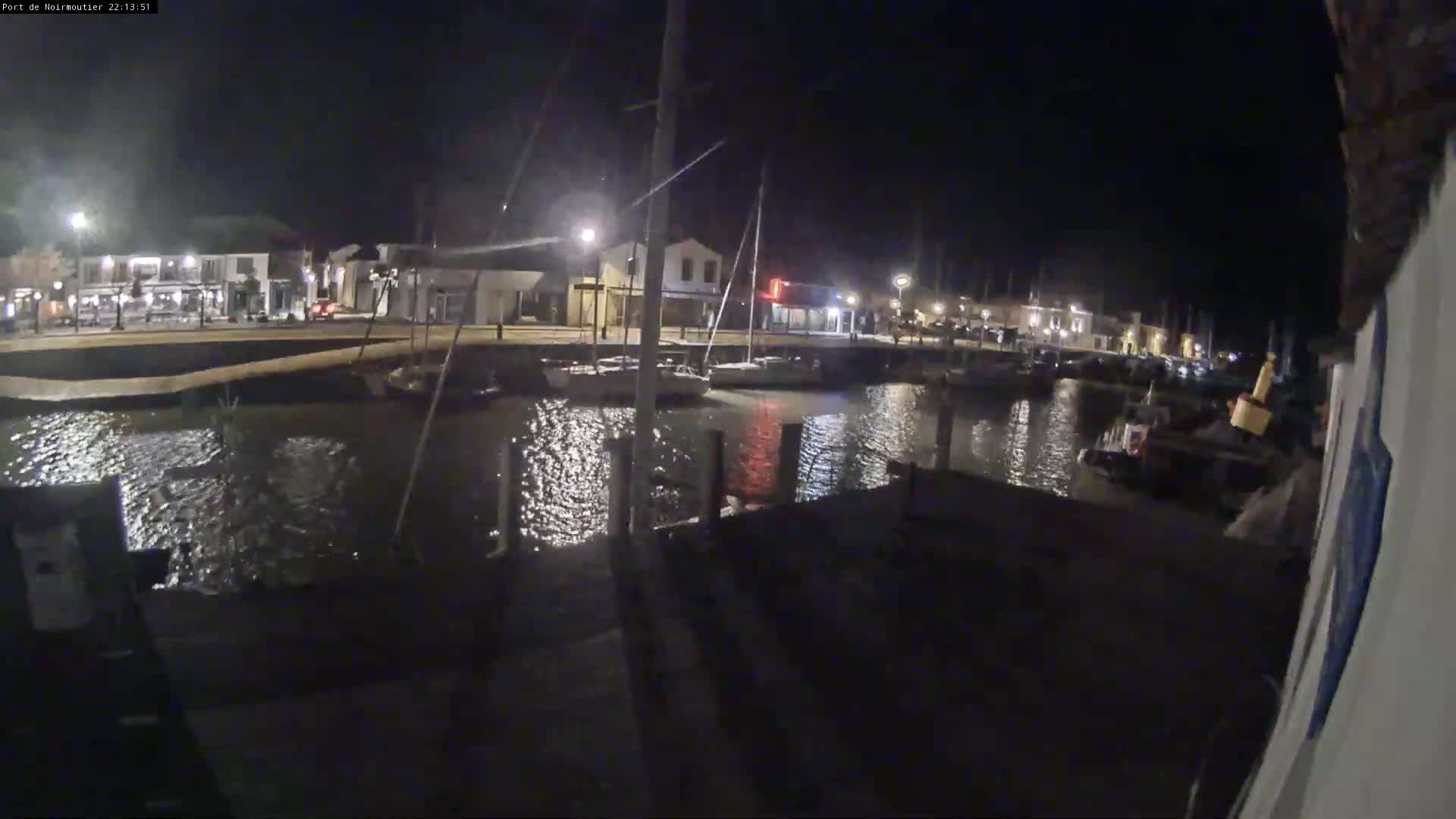 At night, a calm body of water reflects the lights from buildings and docked boats along a waterfront.