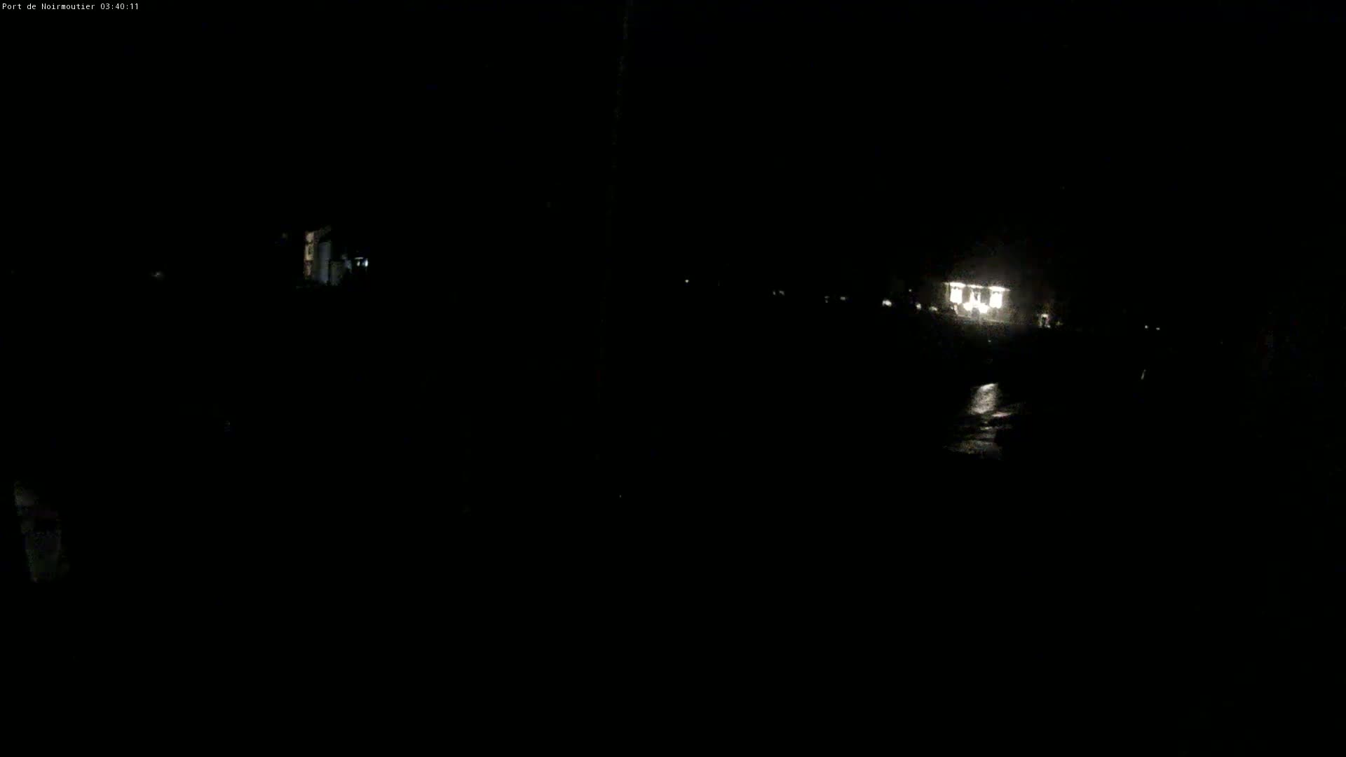 A dimly lit nighttime scene shows a building with lights on in the distance, and a dark, possibly wet, ground in the foreground.