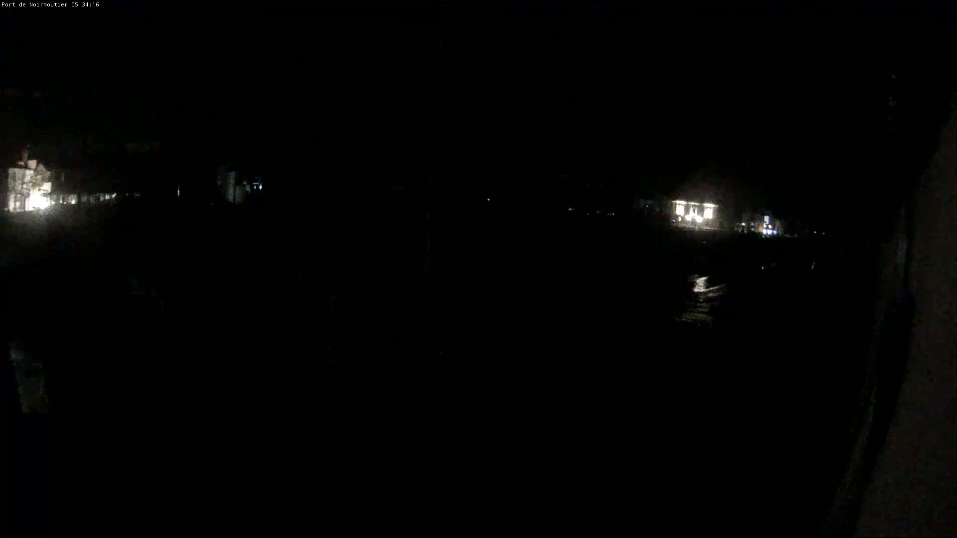 A nighttime, low-light view shows dimly lit buildings and a dark body of water.