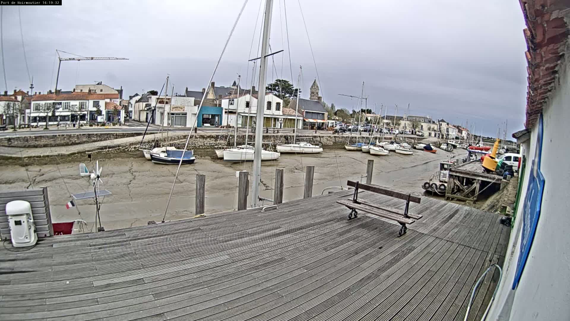 A wooden dock overlooks a harbor with several sailboats at low tide under an overcast sky.