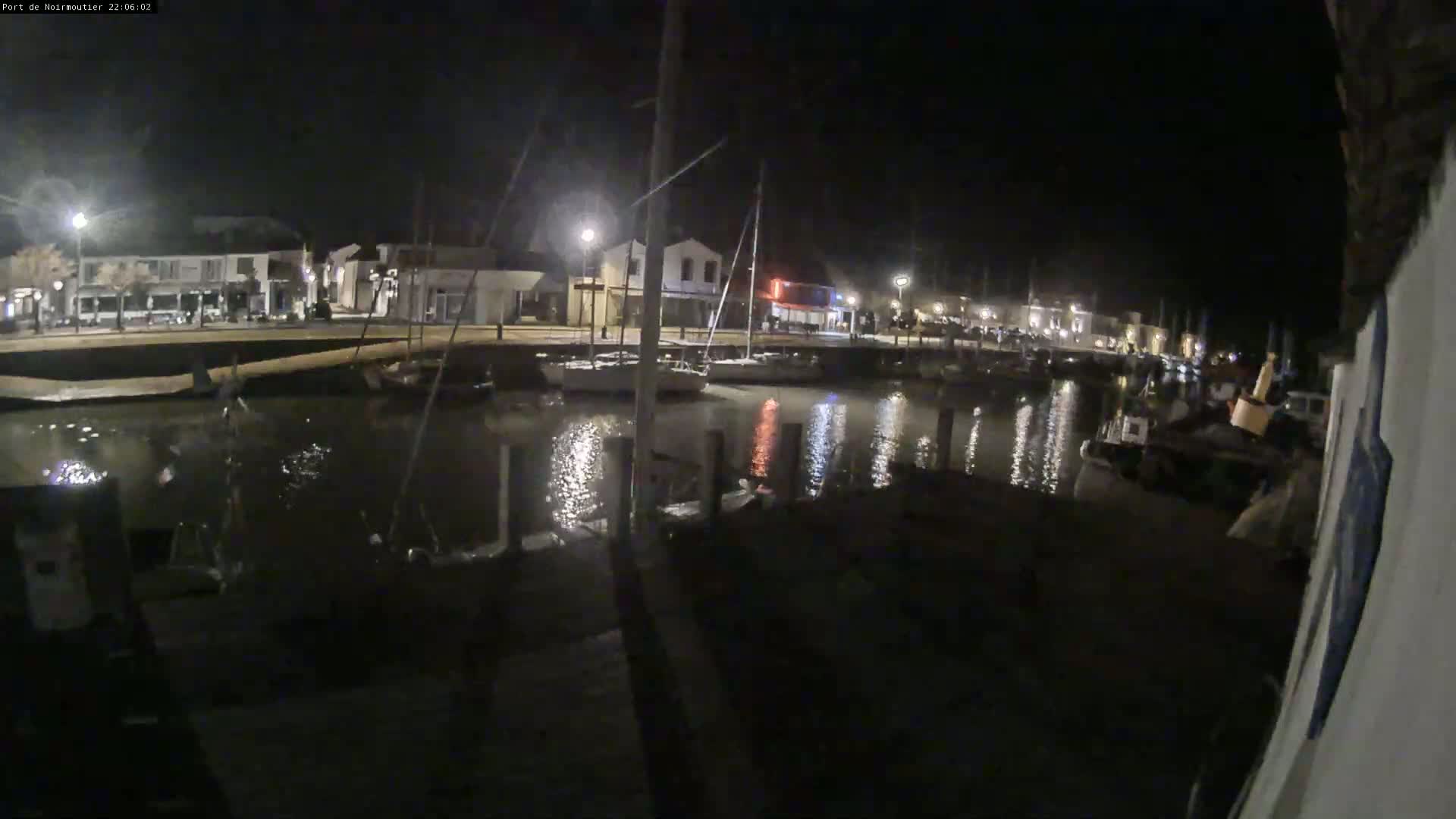 A nighttime view of a calm harbor with boats docked along a waterfront lined with buildings.
