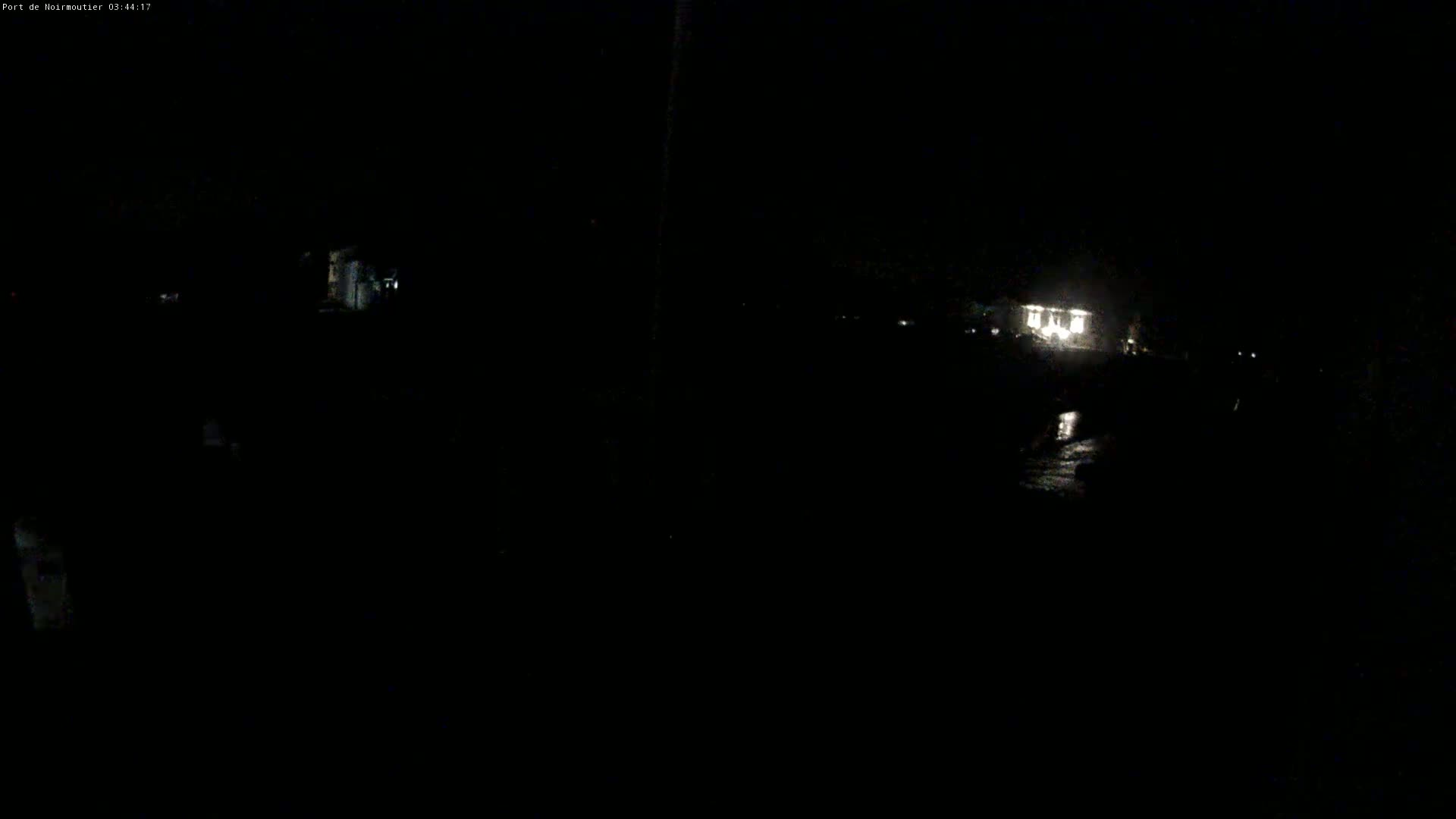 A dark, nighttime scene shows faintly lit buildings and a wet, reflective surface in the distance.