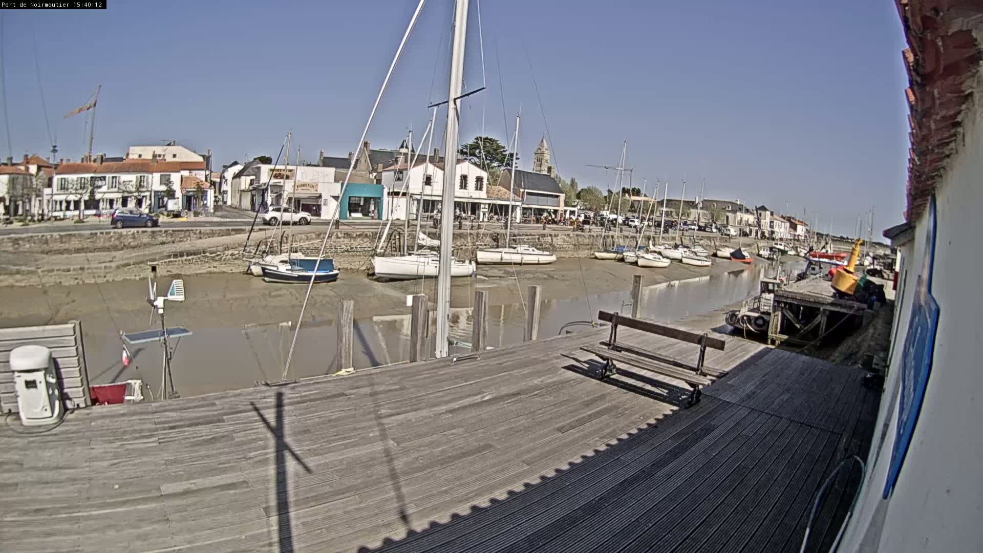 A harbor with sailboats docked at low tide on a sunny day, next to a wooden dock and a small town.