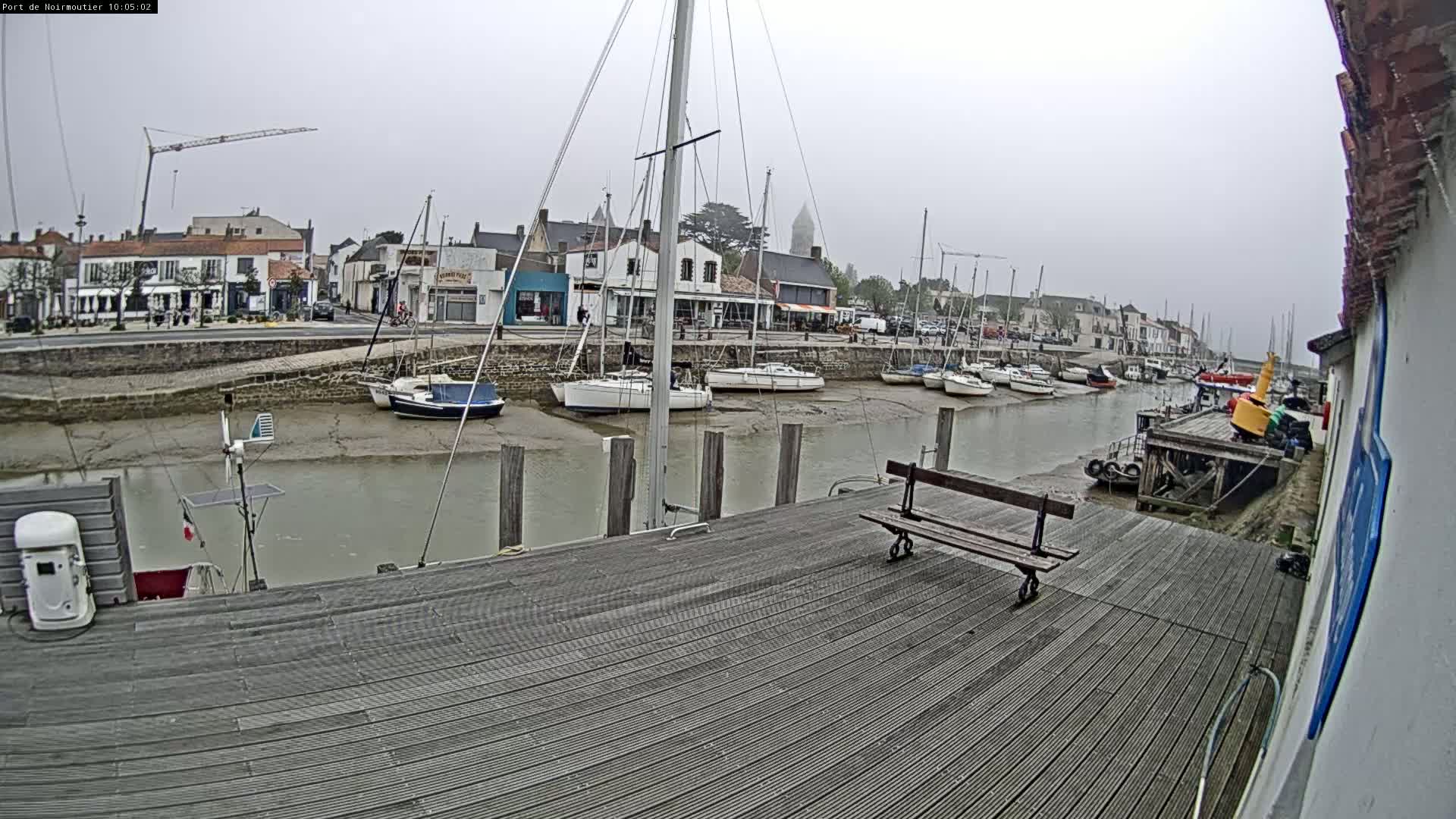 A mostly cloudy day reveals sailboats docked at a harbor next to a town, with a low tide exposing the muddy seabed.