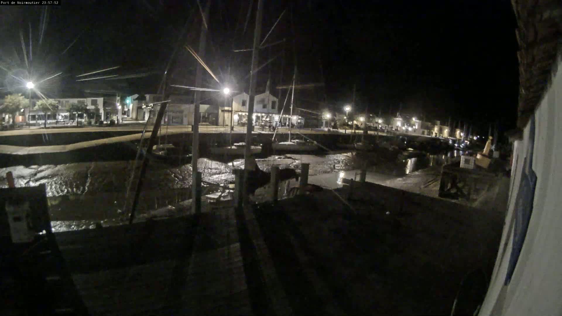 A nighttime view of a harbor with boats docked, low tide exposing a muddy bottom, and buildings illuminated by streetlights.