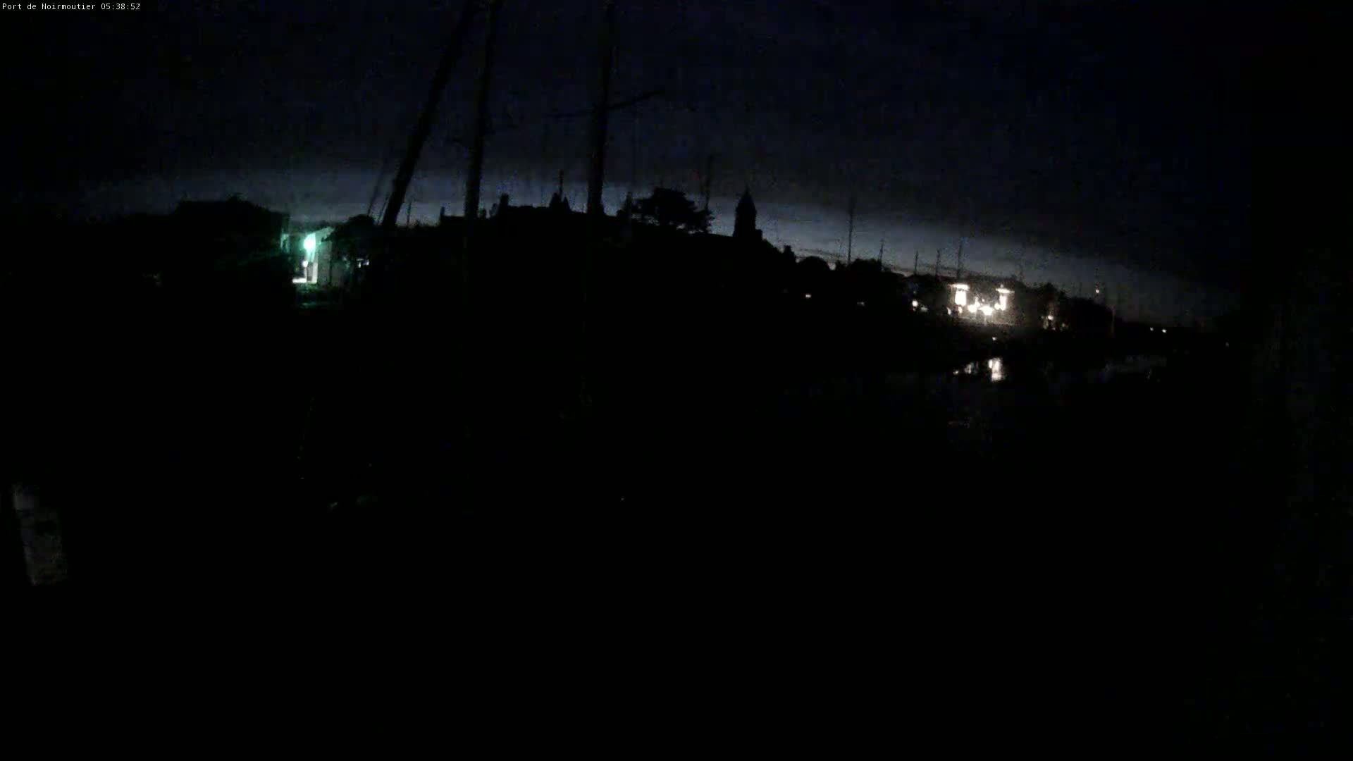 A dark, nighttime scene shows a silhouetted shoreline with a few faint lights and a dark, mostly cloudy sky.