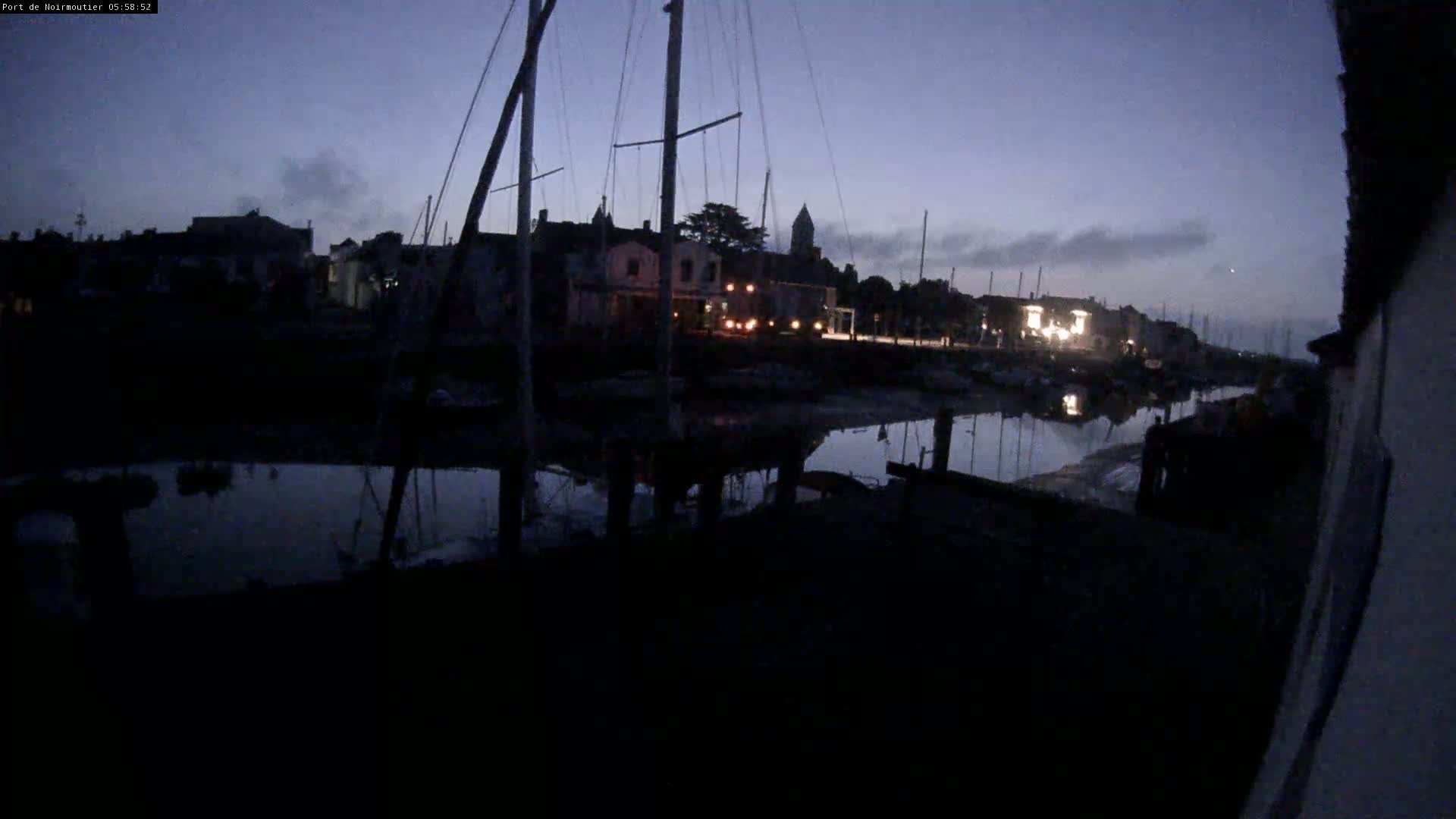 A dark, calm harbor at twilight with several sailboats docked, illuminated by a few distant lights.