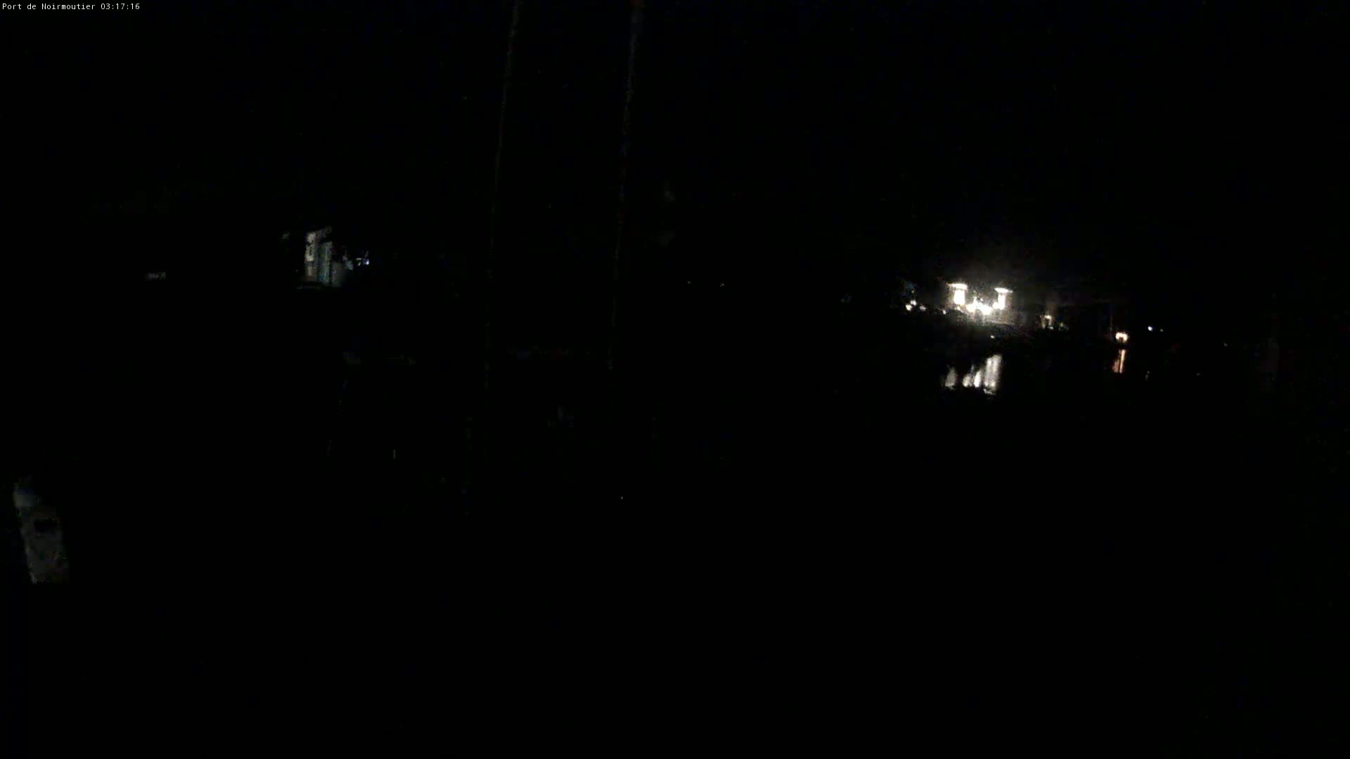 A dark, nighttime scene shows faint lights in the distance reflecting on dark water.