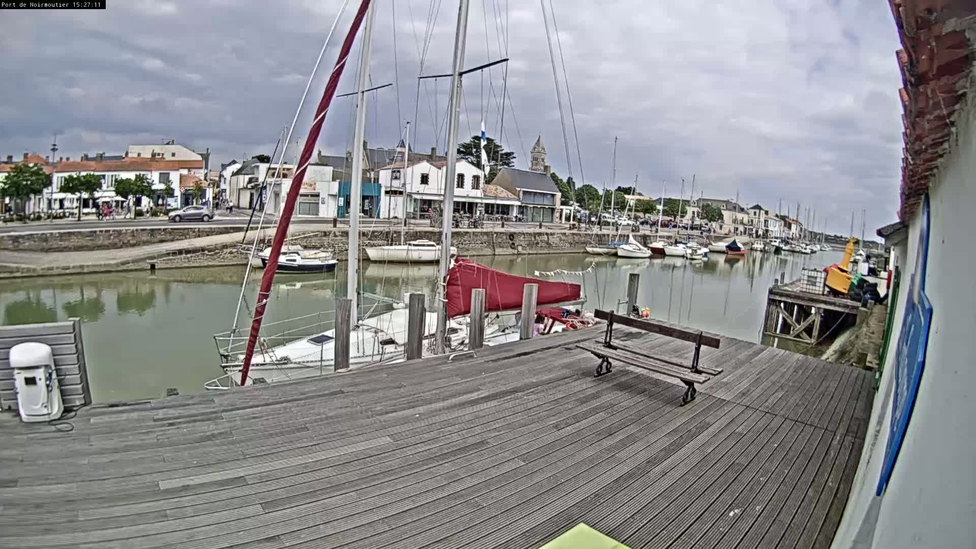 A wooden dock overlooks a calm harbor filled with sailboats under a cloudy sky.