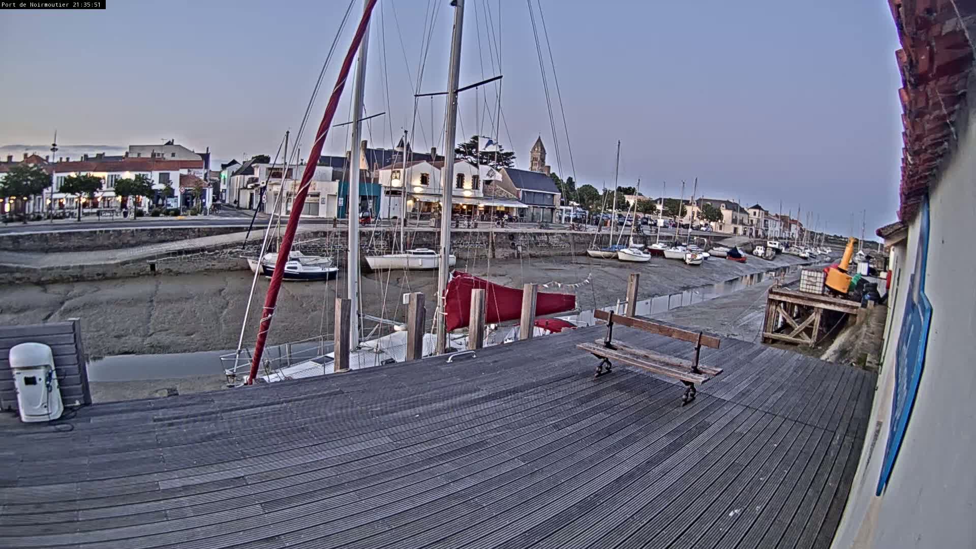 A wooden dock overlooks a harbor at low tide, where several sailboats are moored near a small town under a twilight sky.