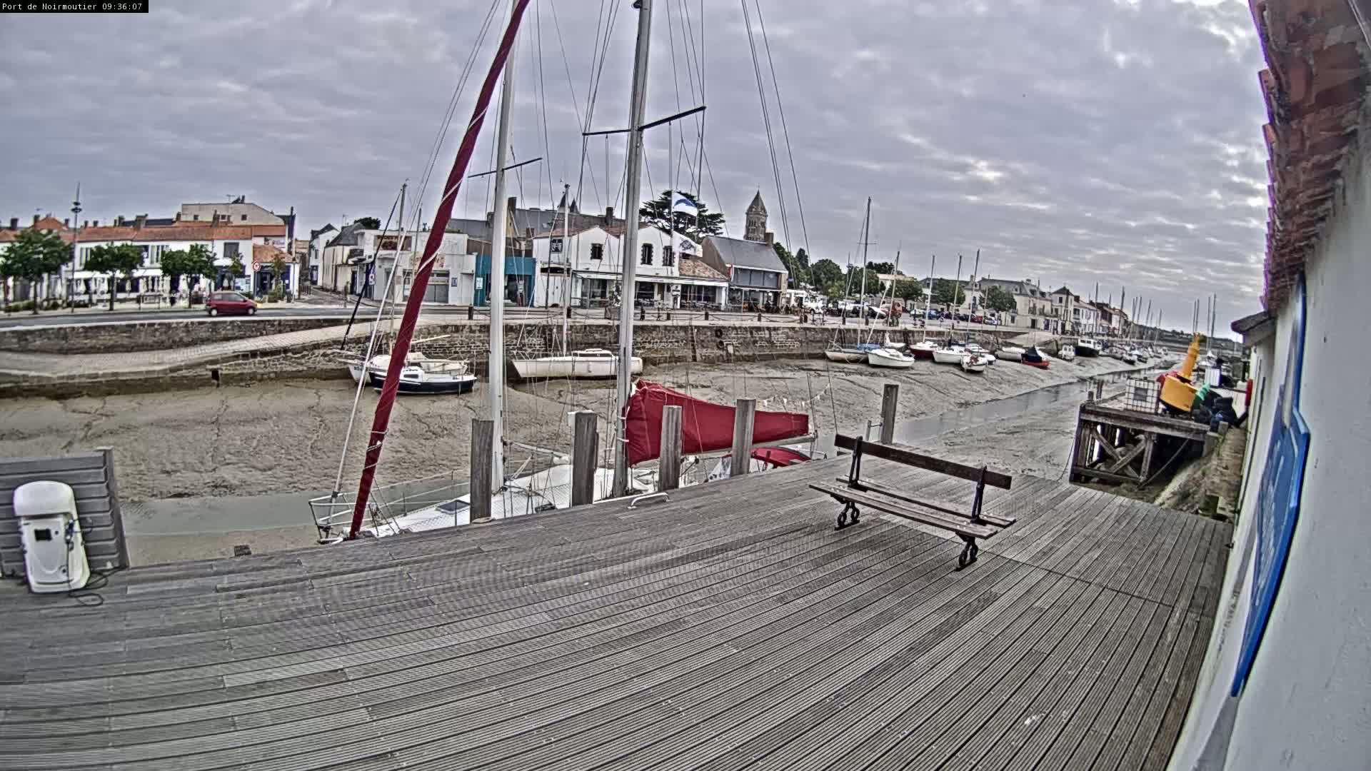 A wooden dock overlooks a harbor with several sailboats at low tide under a cloudy sky.