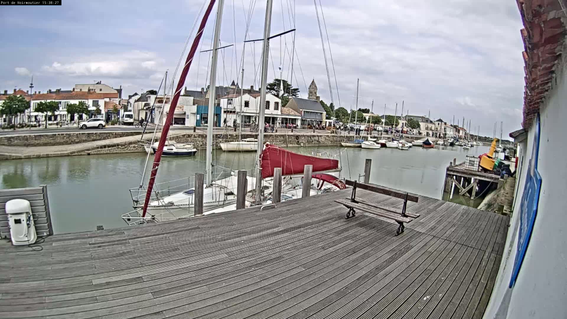 A wooden dock with a bench overlooks a calm harbor filled with sailboats on an overcast day.