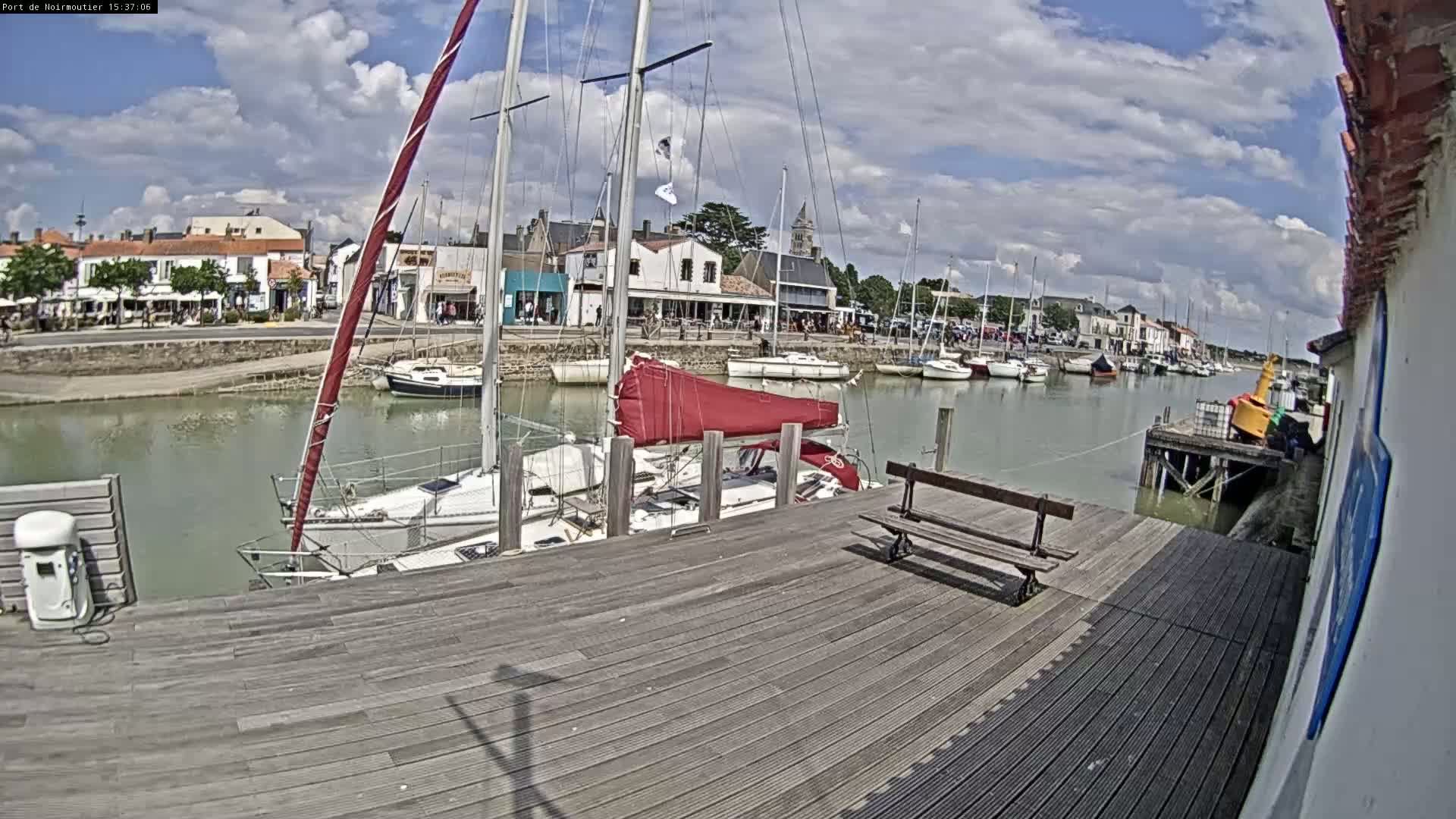 A wooden dock overlooks a harbor filled with sailboats under a partly cloudy sky.