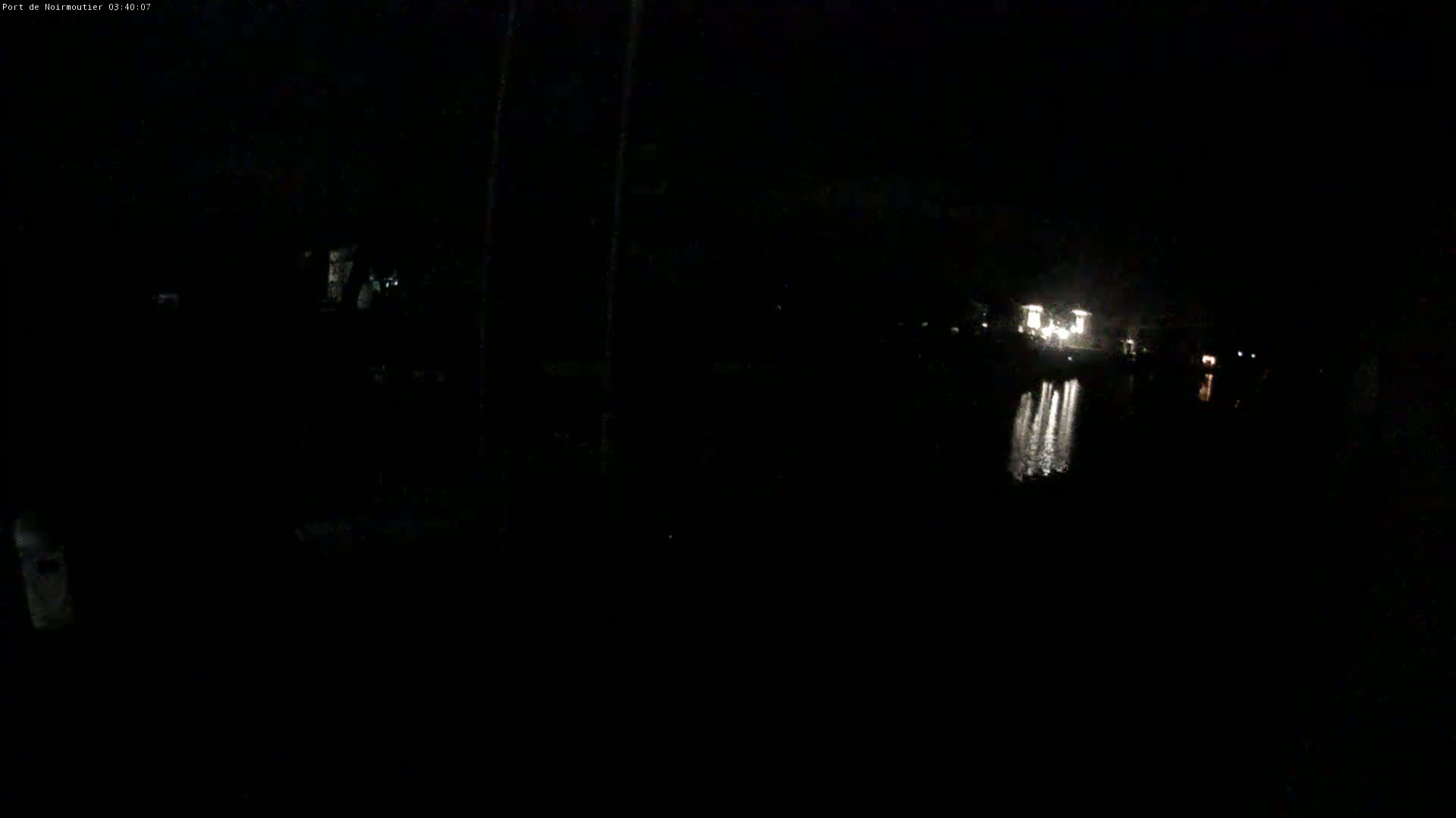 A dark nighttime scene shows a body of water reflecting lights from a distant structure.