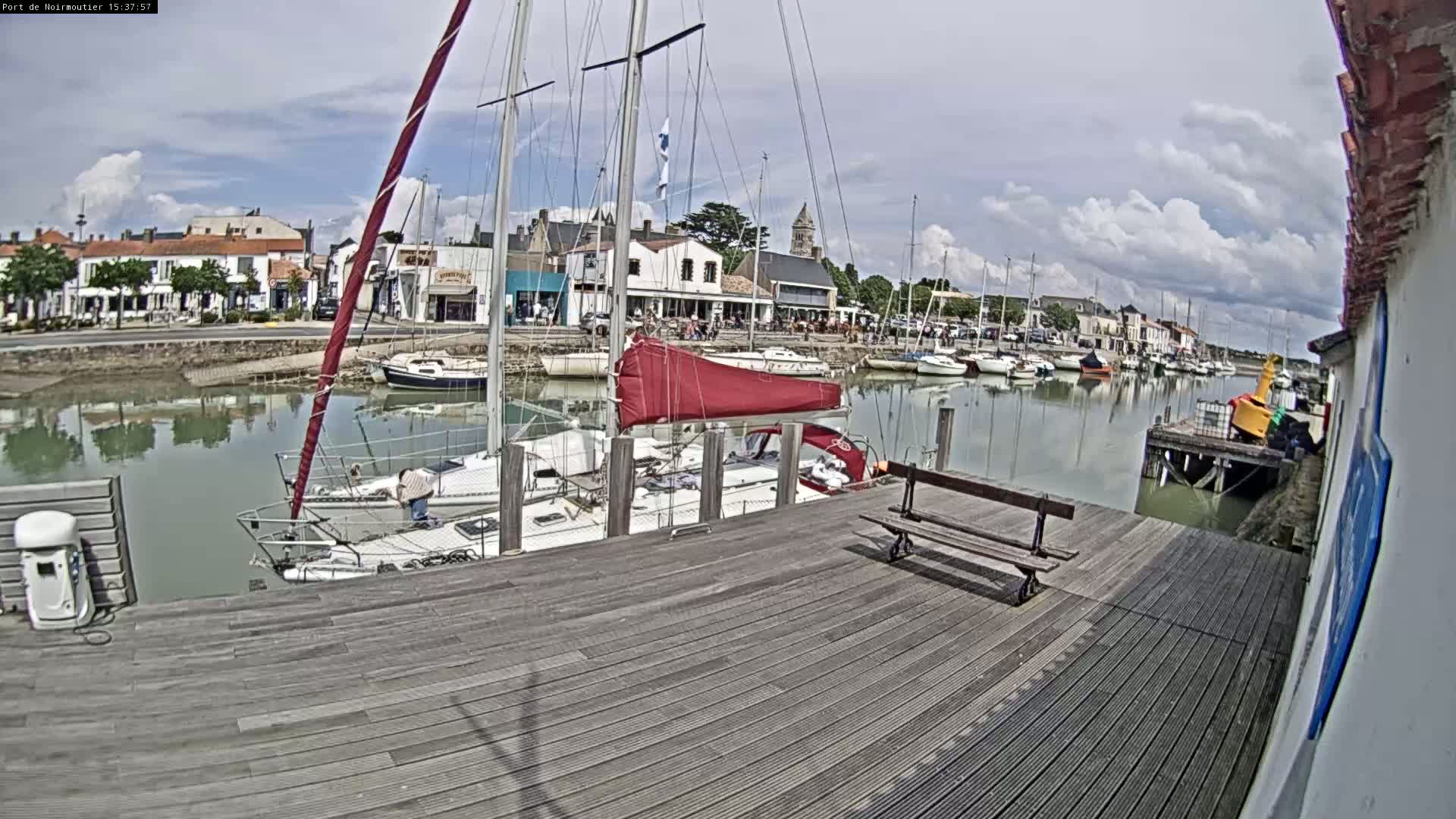 A wooden dock overlooks a calm harbor filled with sailboats on a partly cloudy day.
