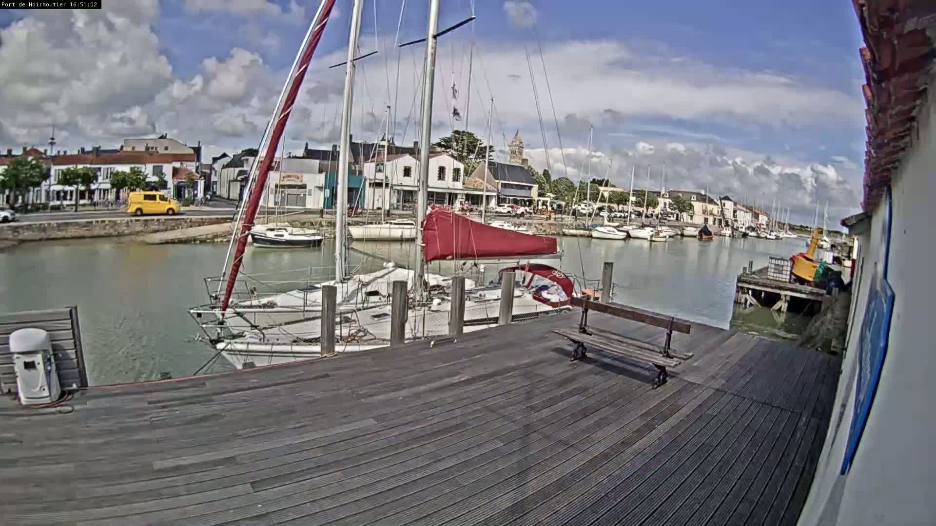 A wooden dock overlooks a harbor filled with sailboats under a partly cloudy sky.