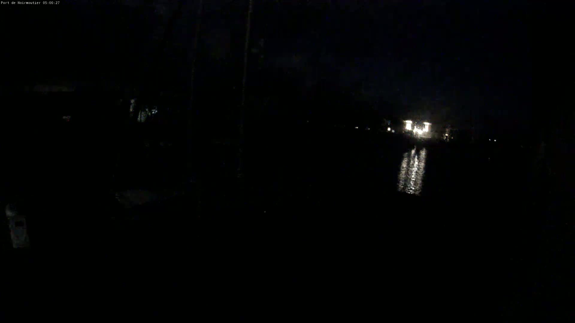 A dark, nighttime scene shows a body of water reflecting lights from a distant structure.