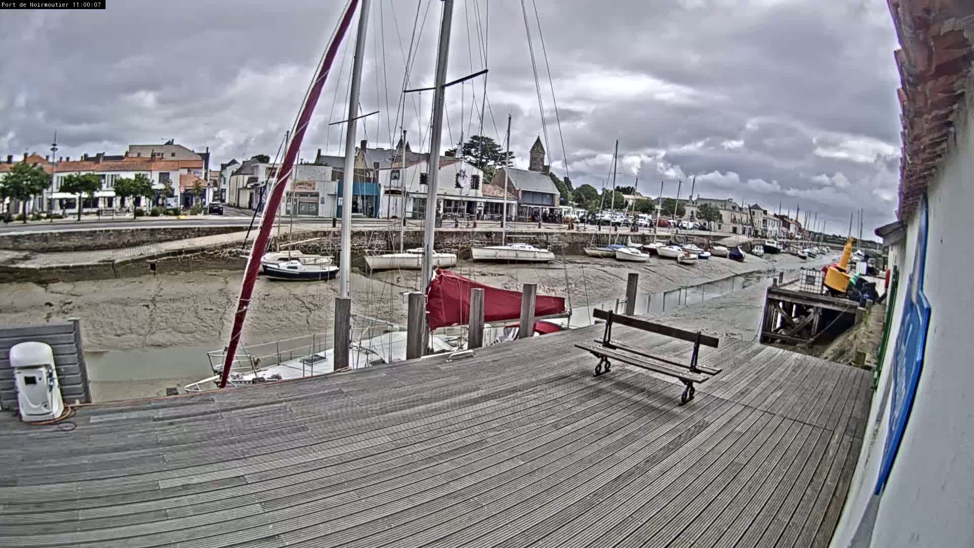 A wooden dock overlooks a harbor with numerous sailboats at low tide under a cloudy sky.