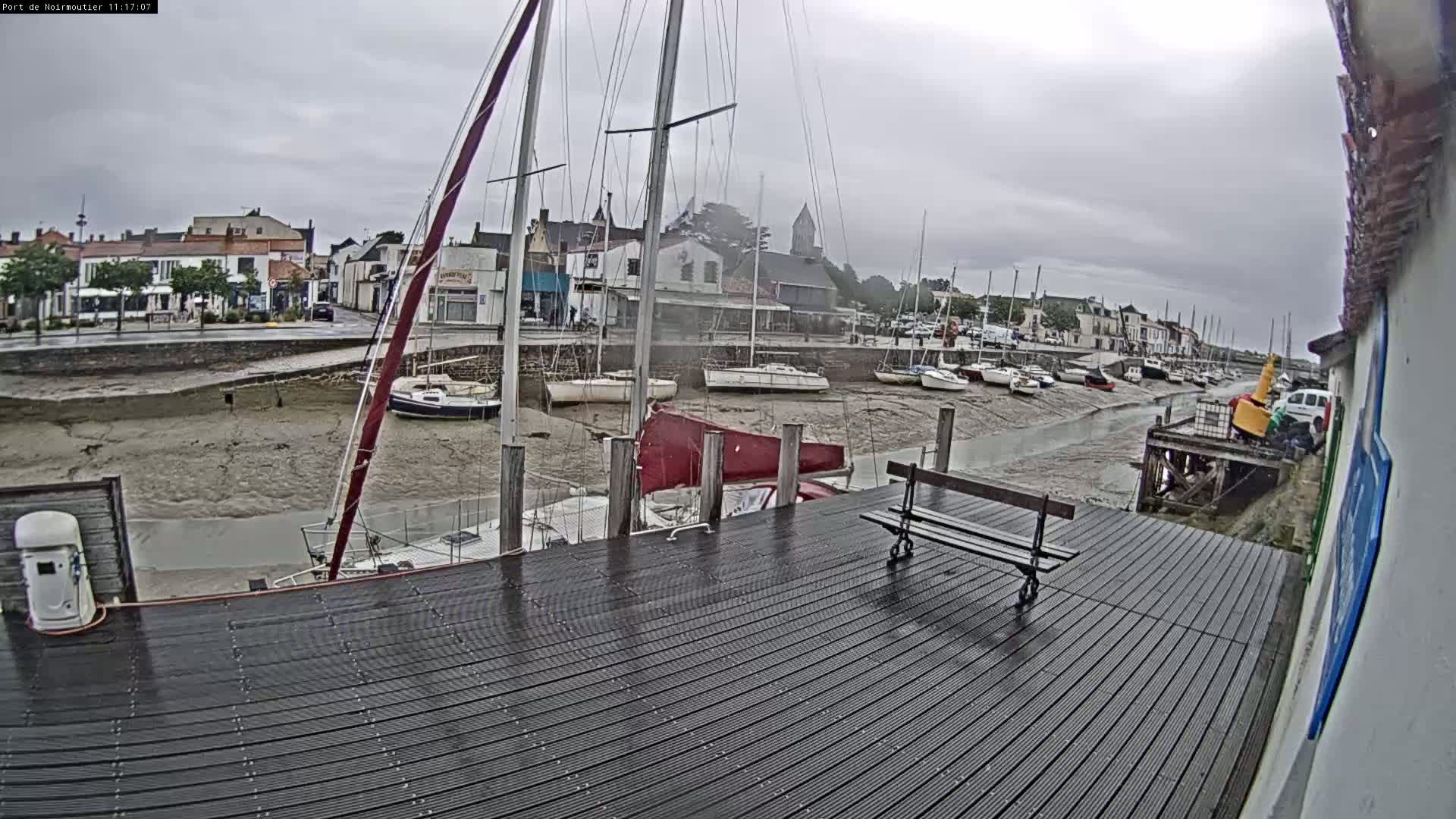 A wet wooden dock overlooks a harbor with sailboats at low tide under an overcast sky.
