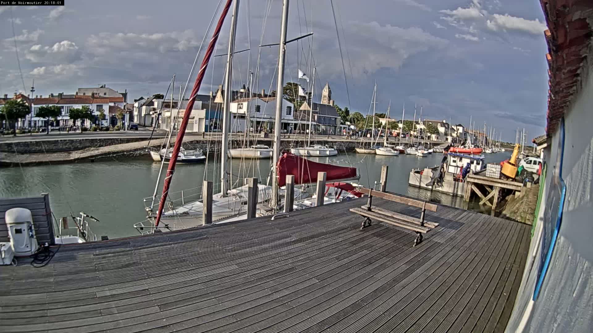 A partly cloudy day reveals a harbor filled with sailboats and a few small motorboats moored along a wooden dock.