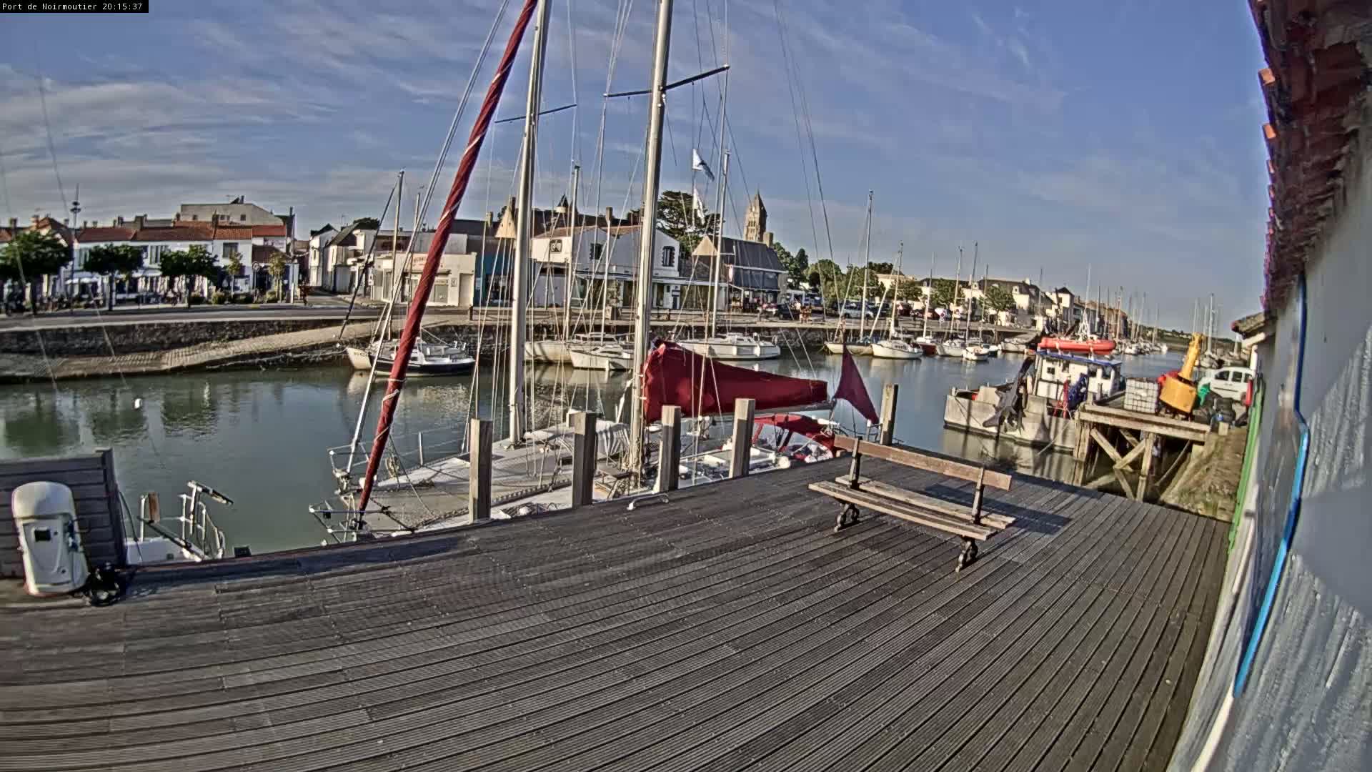 A harbor filled with sailboats under a mostly sunny sky, viewed from a wooden dock.