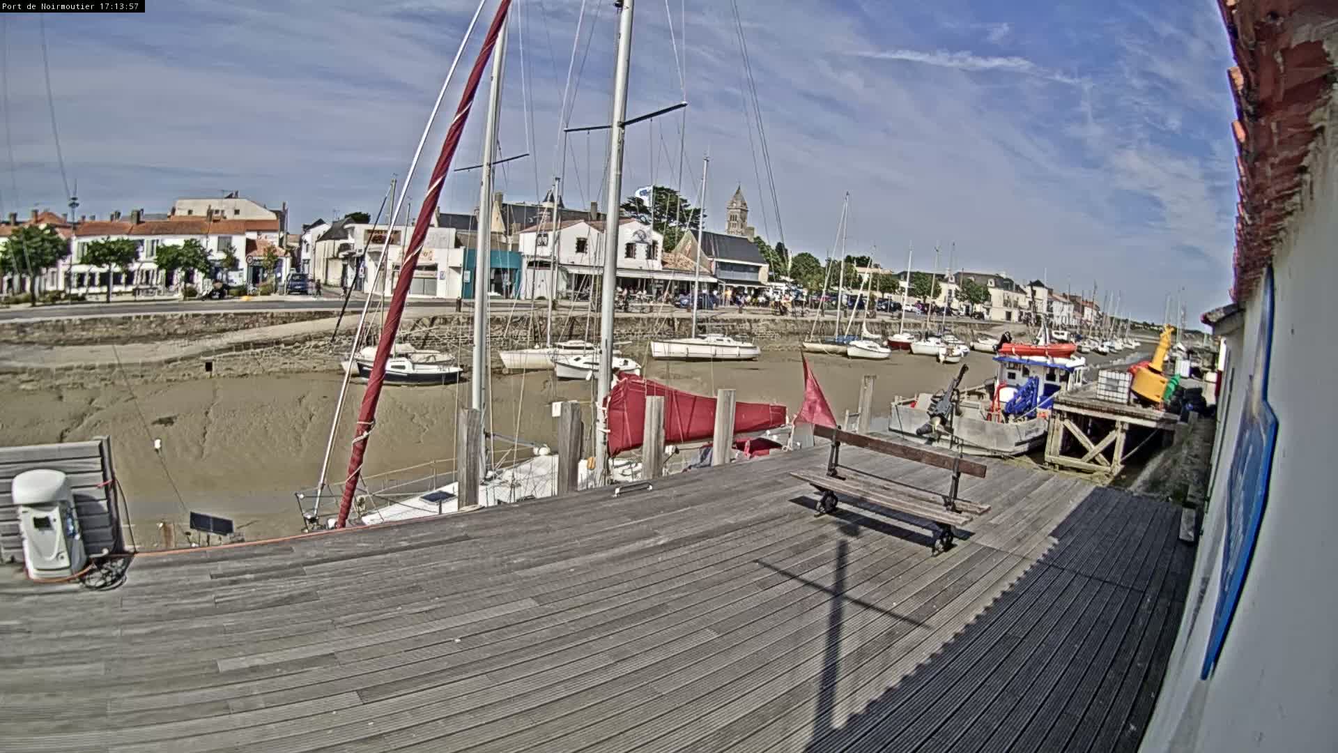 A mostly sunny day reveals a harbor with numerous sailboats docked in shallow, muddy water, viewed from a wooden dock.