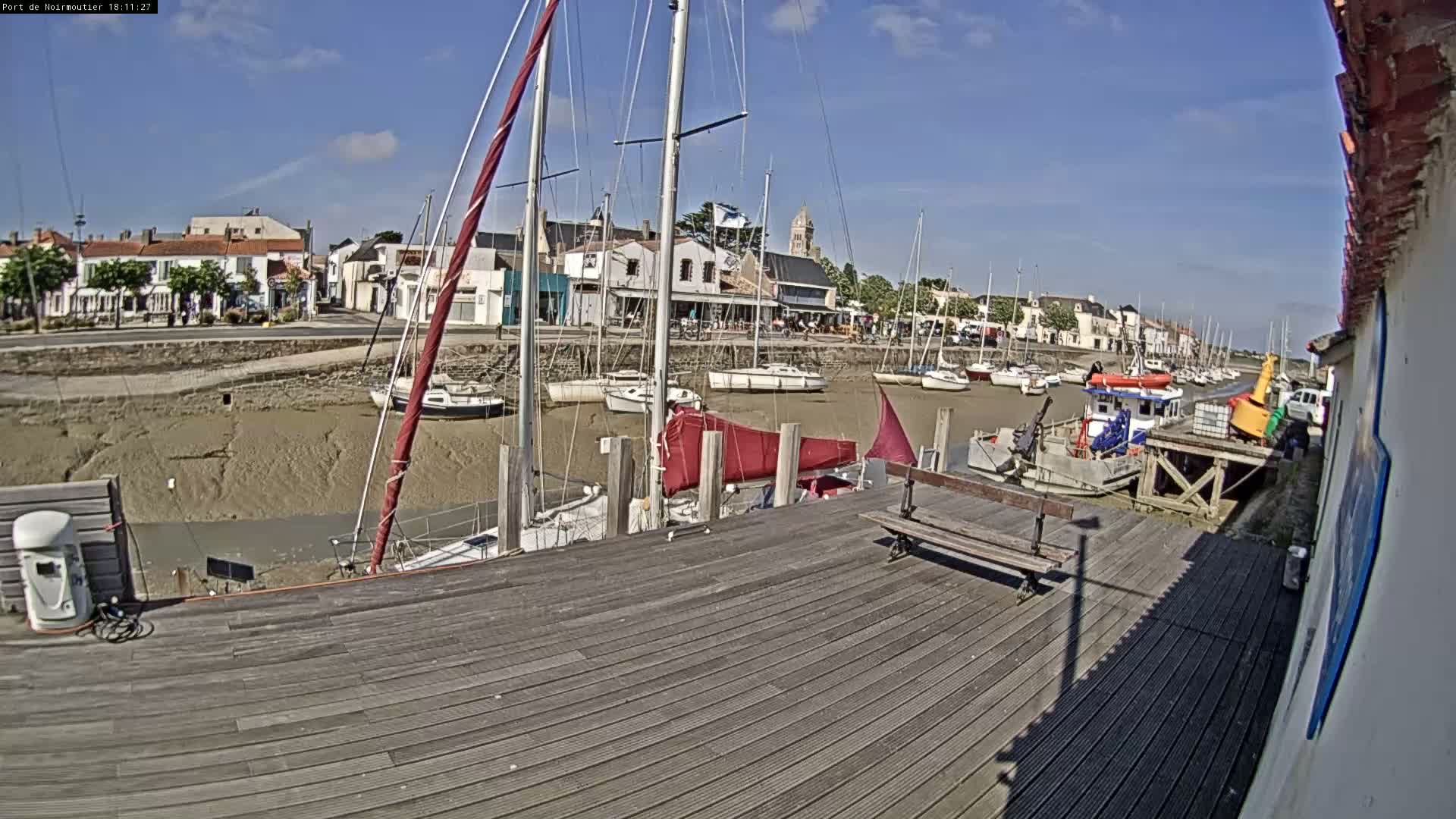 A wooden dock overlooks a harbor with numerous sailboats at low tide under a sunny sky.