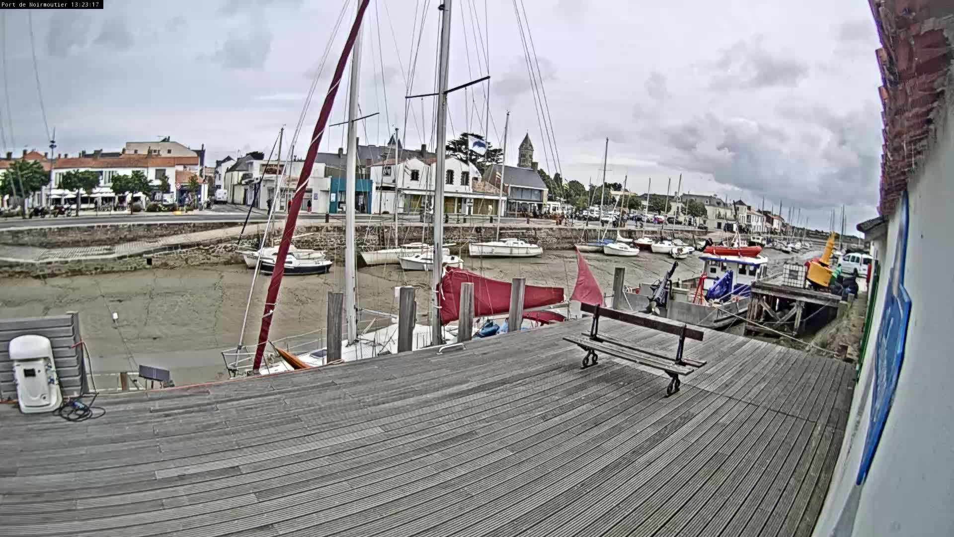 A wooden dock overlooks a harbor with sailboats at low tide under a cloudy sky.