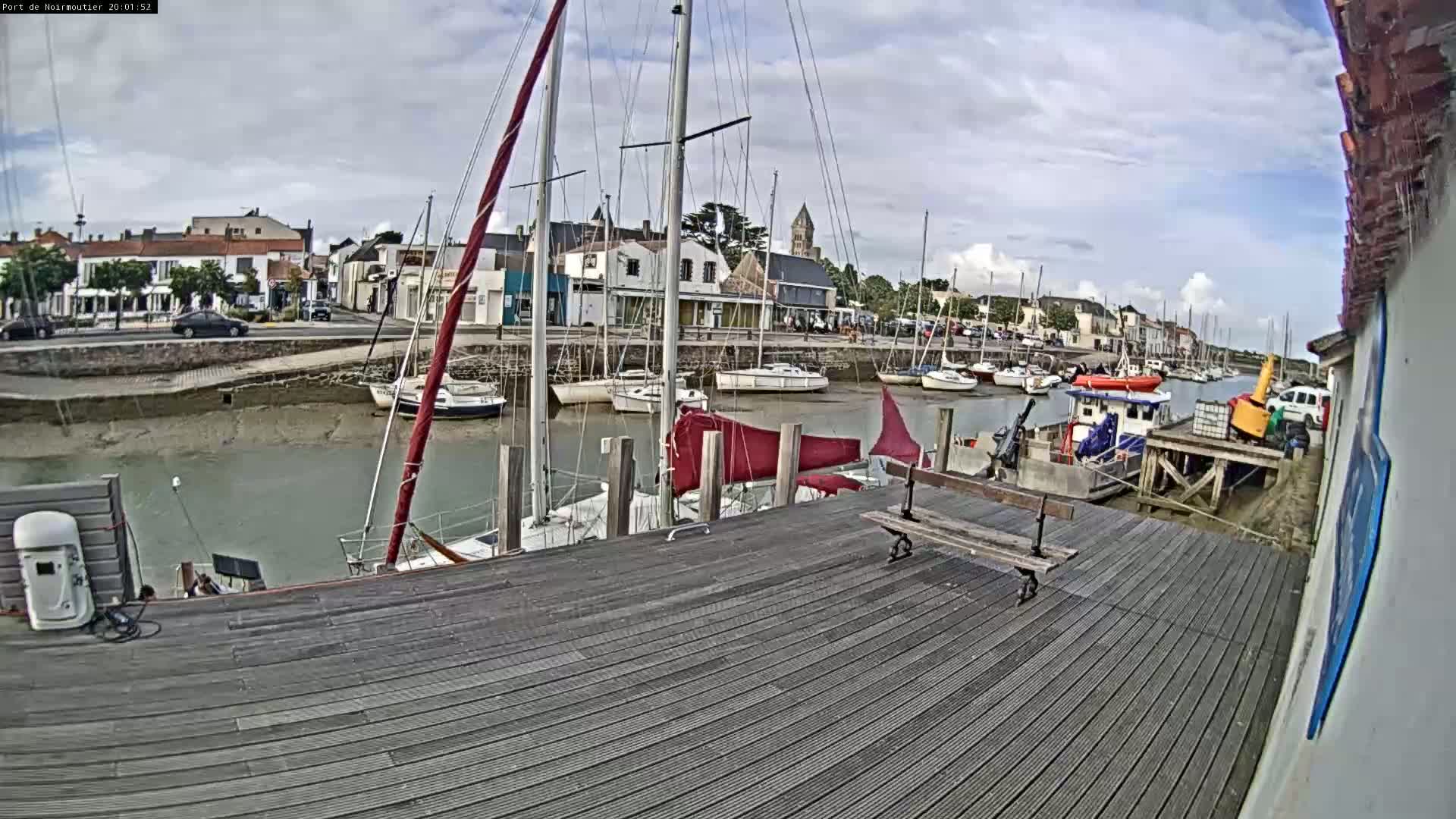 A wooden dock overlooks a harbor filled with sailboats at low tide under a partly cloudy sky.