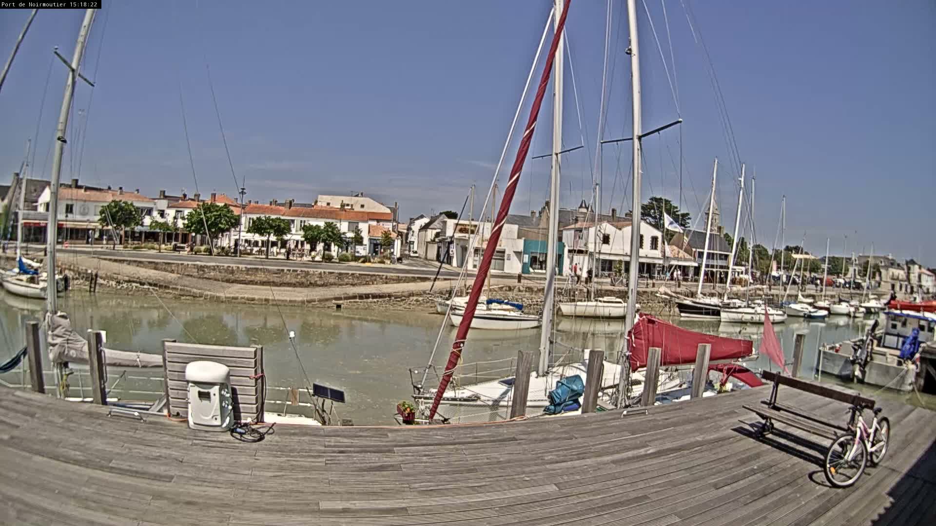 A marina filled with sailboats under a clear blue sky, with a town of light-colored buildings visible in the background.