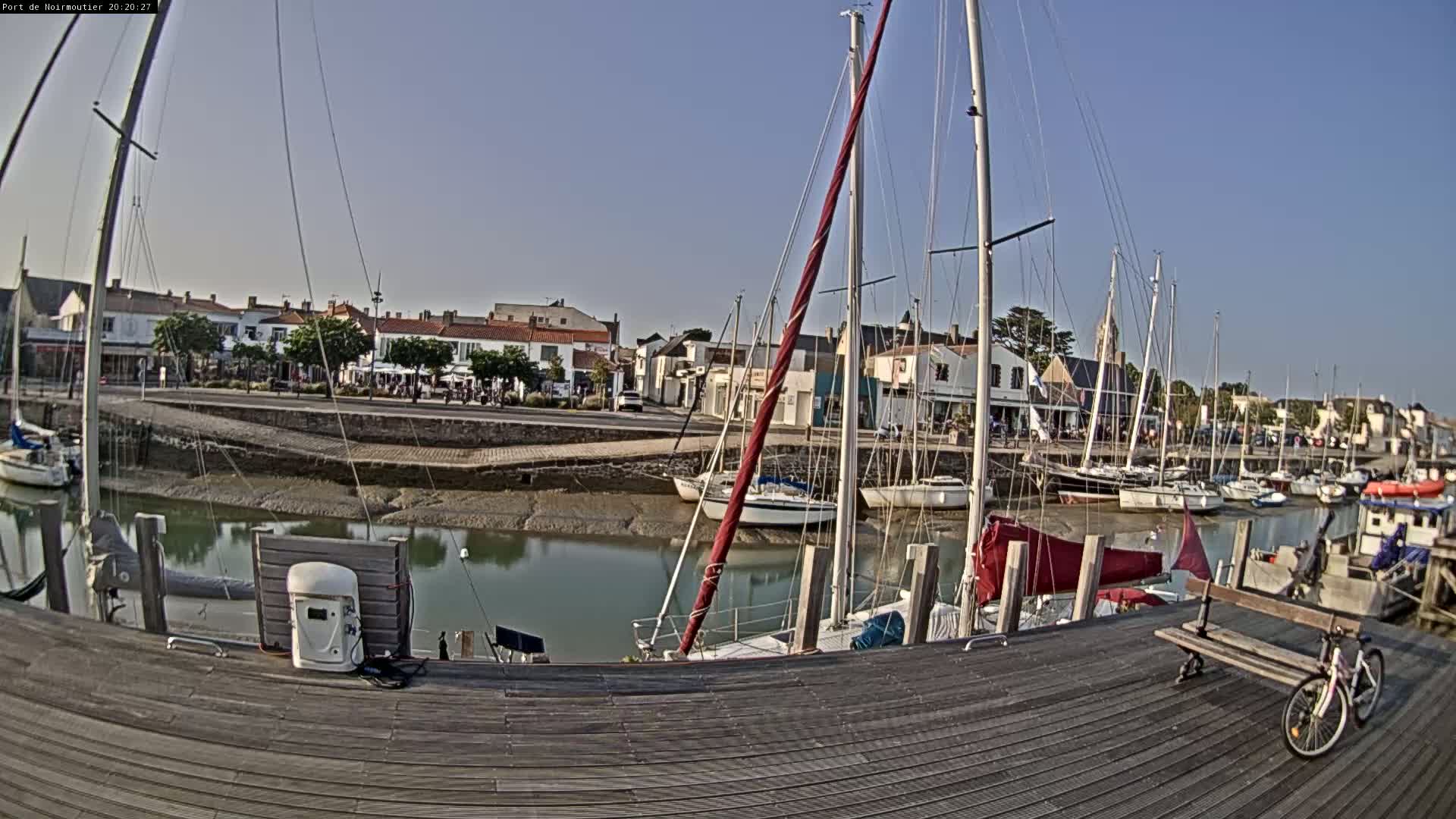 A marina with sailboats docked along a wooden pier, under a clear, sunny sky, on a low tide.
