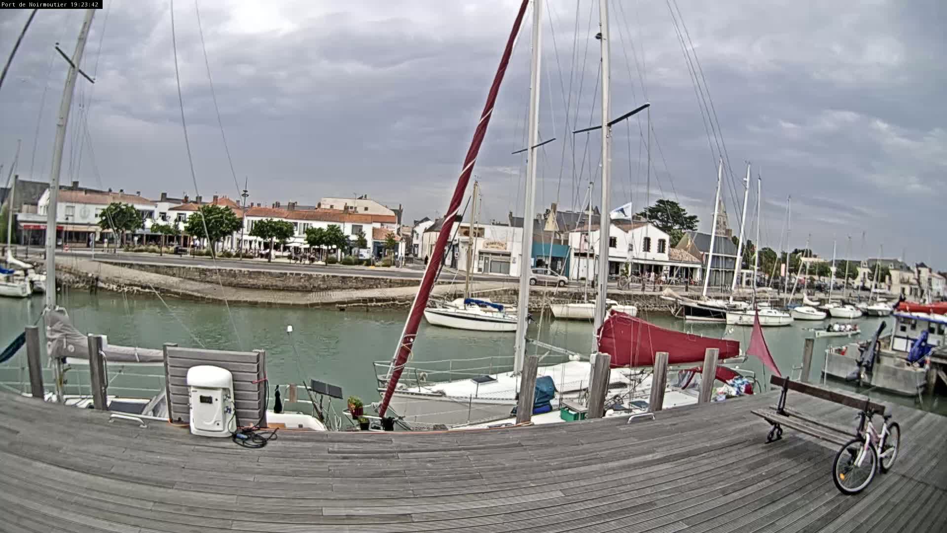 A harbor with numerous sailboats docked along a wooden pier under a cloudy sky.