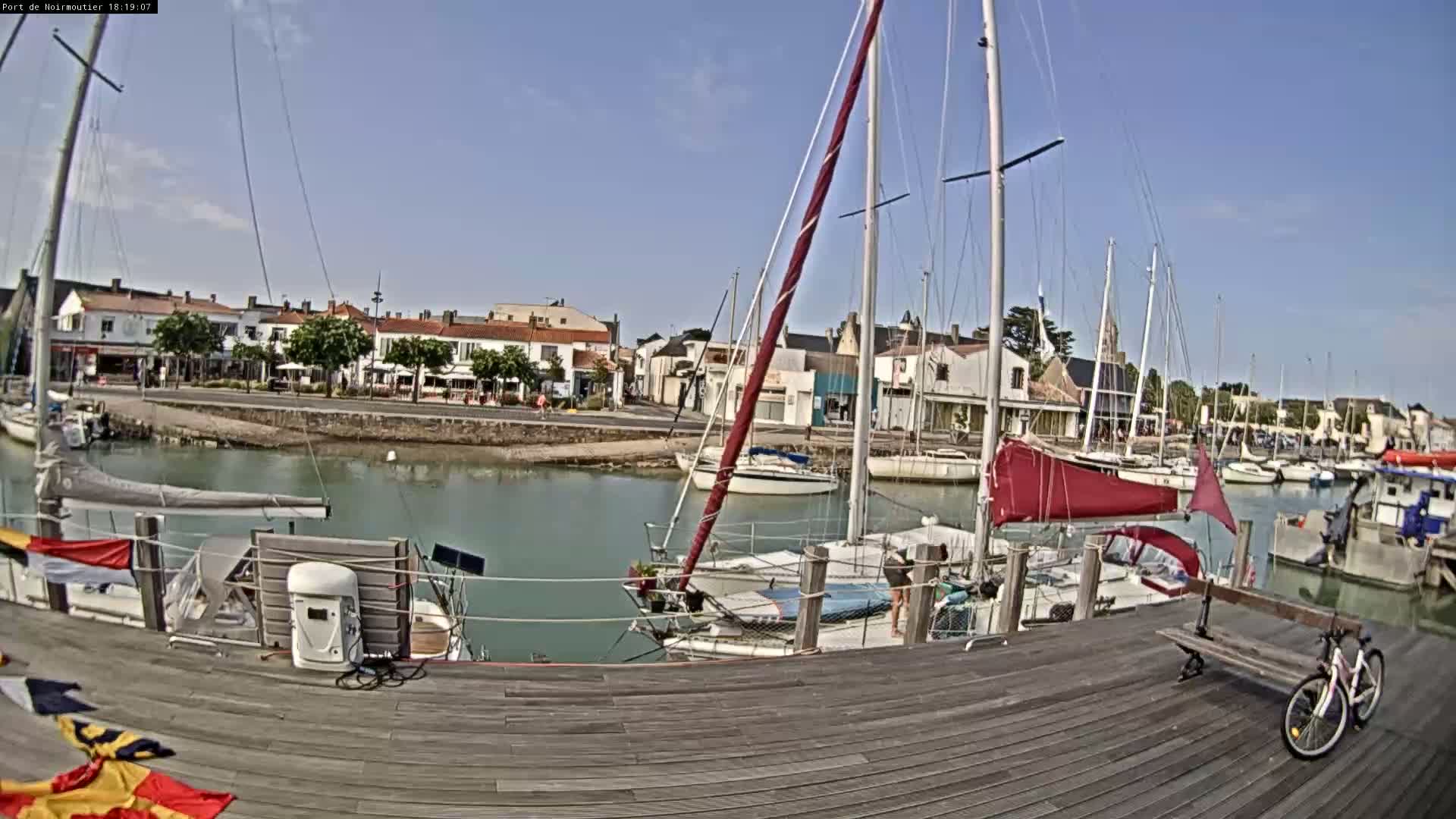 A calm harbor with numerous sailboats docked along a wooden boardwalk on a sunny day.