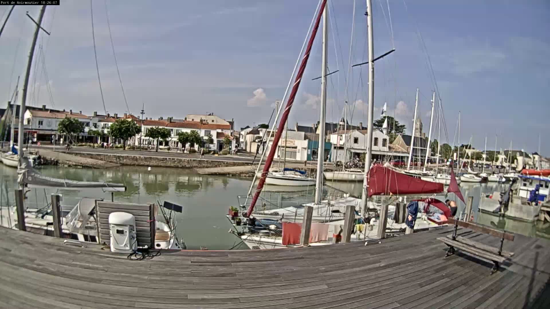 A marina with sailboats docked along a wooden pier on a partly sunny day.