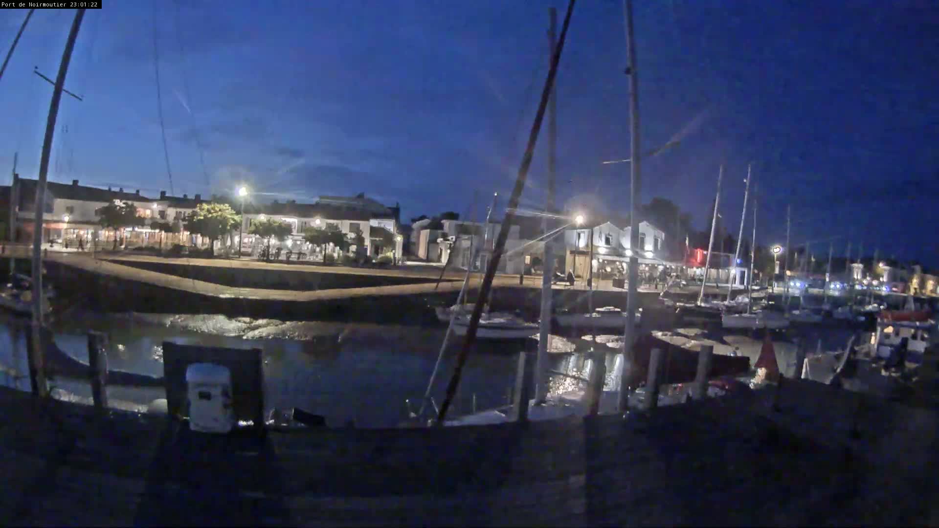 A harbor filled with sailboats under a cloudy sky, with a wooden dock in the foreground and buildings lining the waterfront.