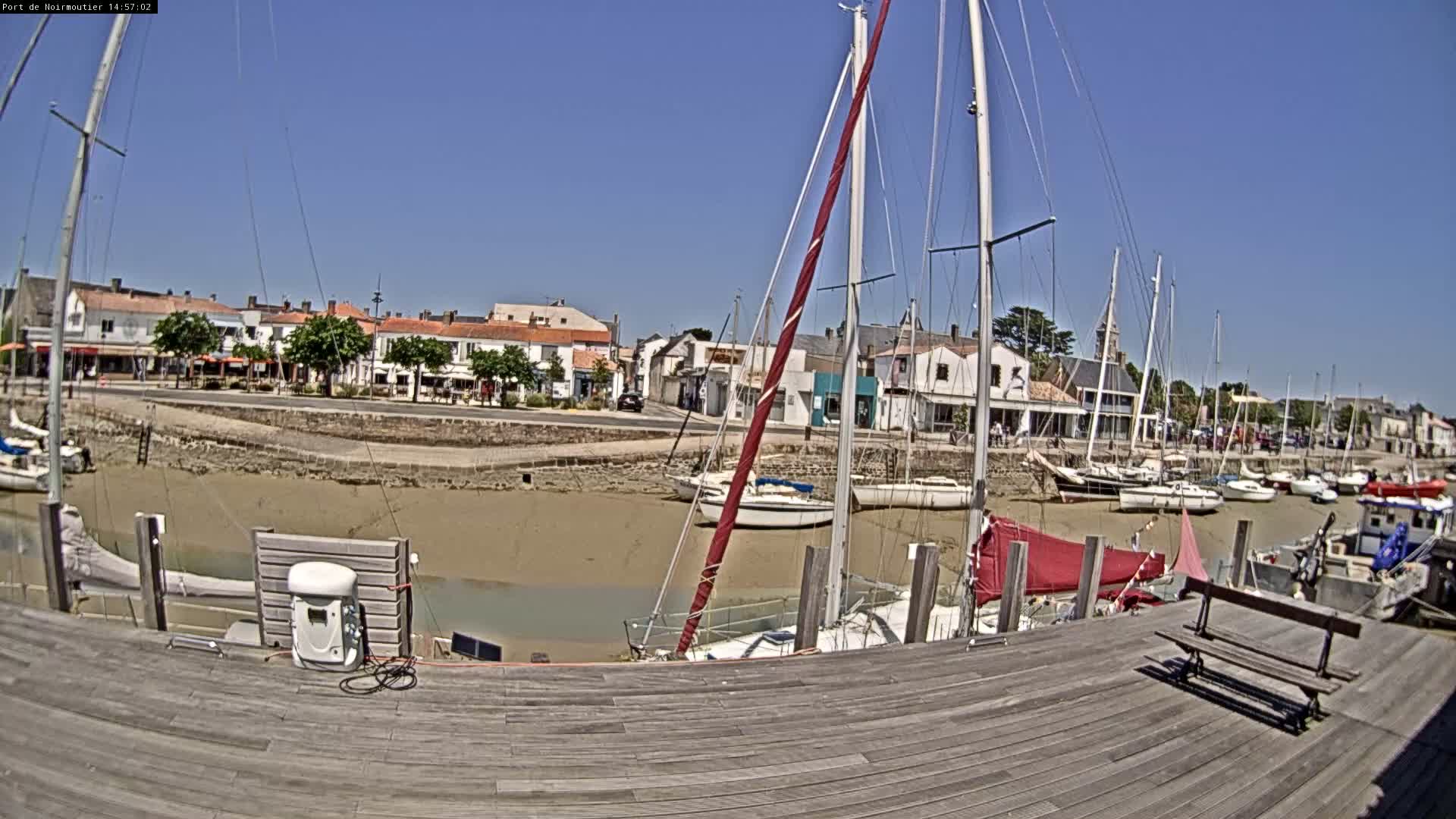 A sunny day at a harbor shows sailboats docked in shallow, muddy water in front of a waterfront town.