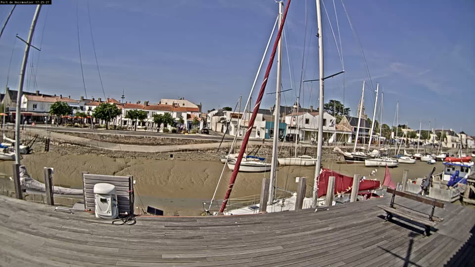 A wooden dock overlooks a harbor filled with sailboats at low tide under a clear blue sky.