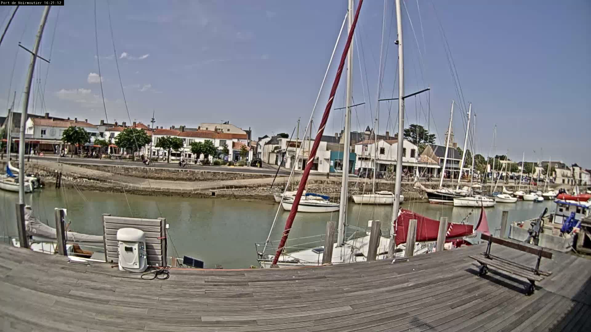 A harbor filled with sailboats on a sunny day, viewed from a wooden dock.