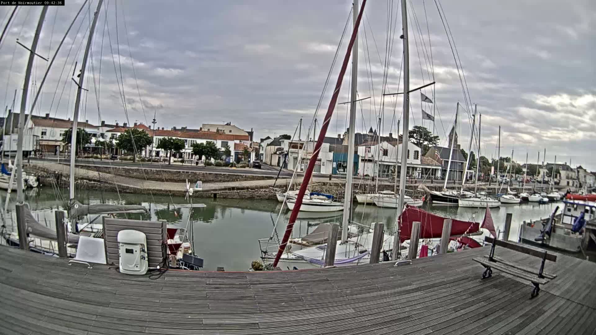 A harbor filled with sailboats and small motorboats under a cloudy sky, viewed from a wooden dock.