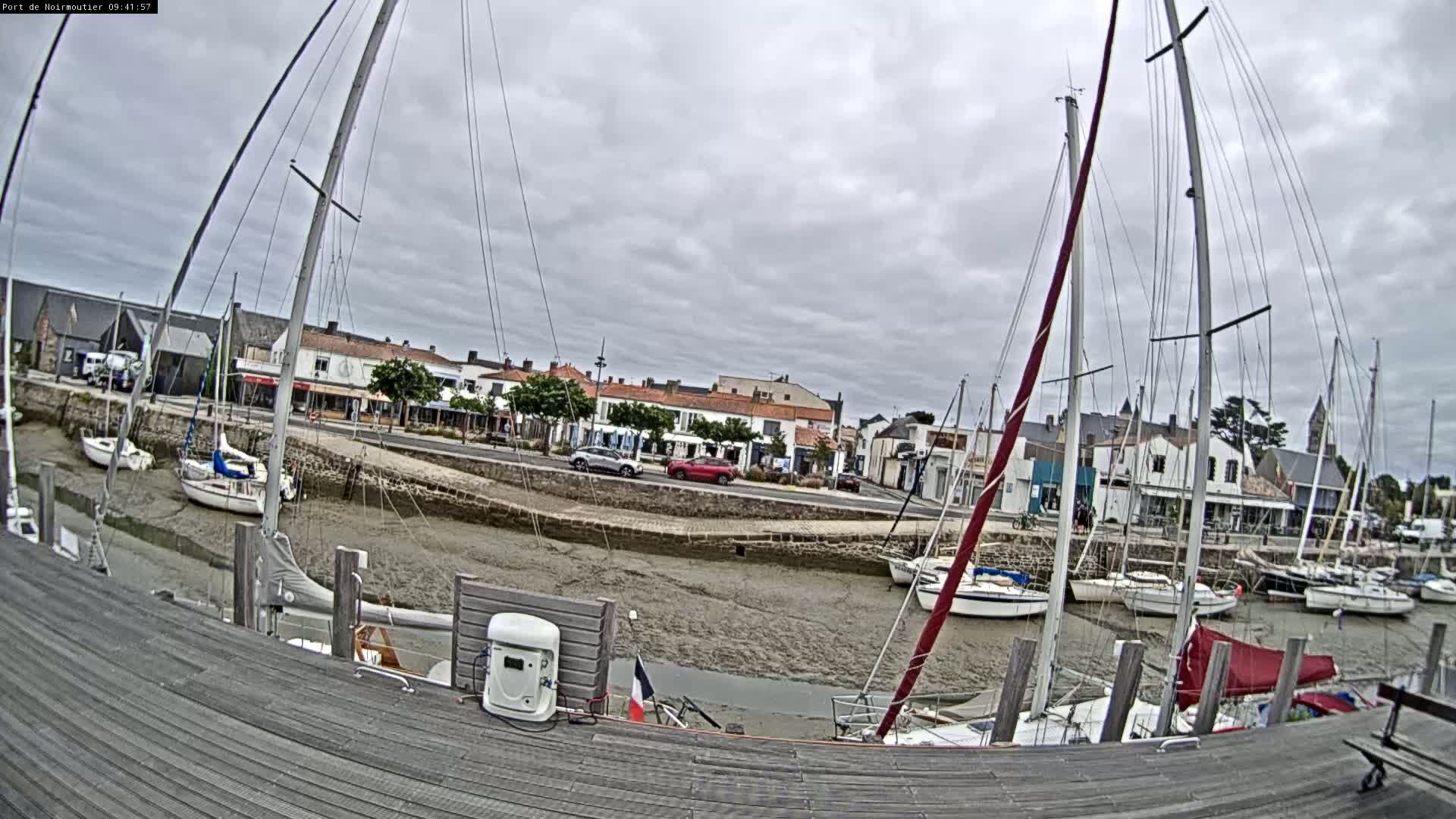 Several sailboats are docked in a harbor with exposed mudflats, under a cloudy sky.