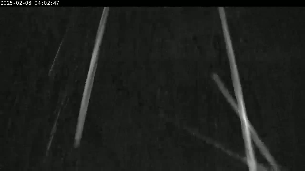 A nighttime, low-light image shows several bright streaks of light against a dark background, possibly headlights from vehicles on a road.