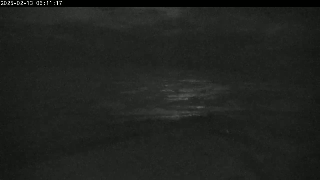 A dark, low-light outdoor scene shows a mostly cloudy night sky with a faint glow near the horizon.