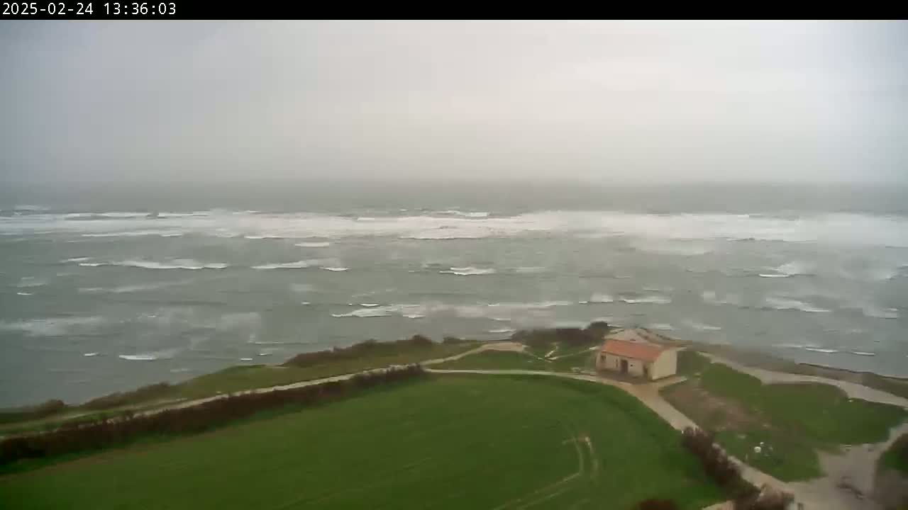 A small building sits on a grassy hill overlooking a choppy, gray sea under an overcast sky.