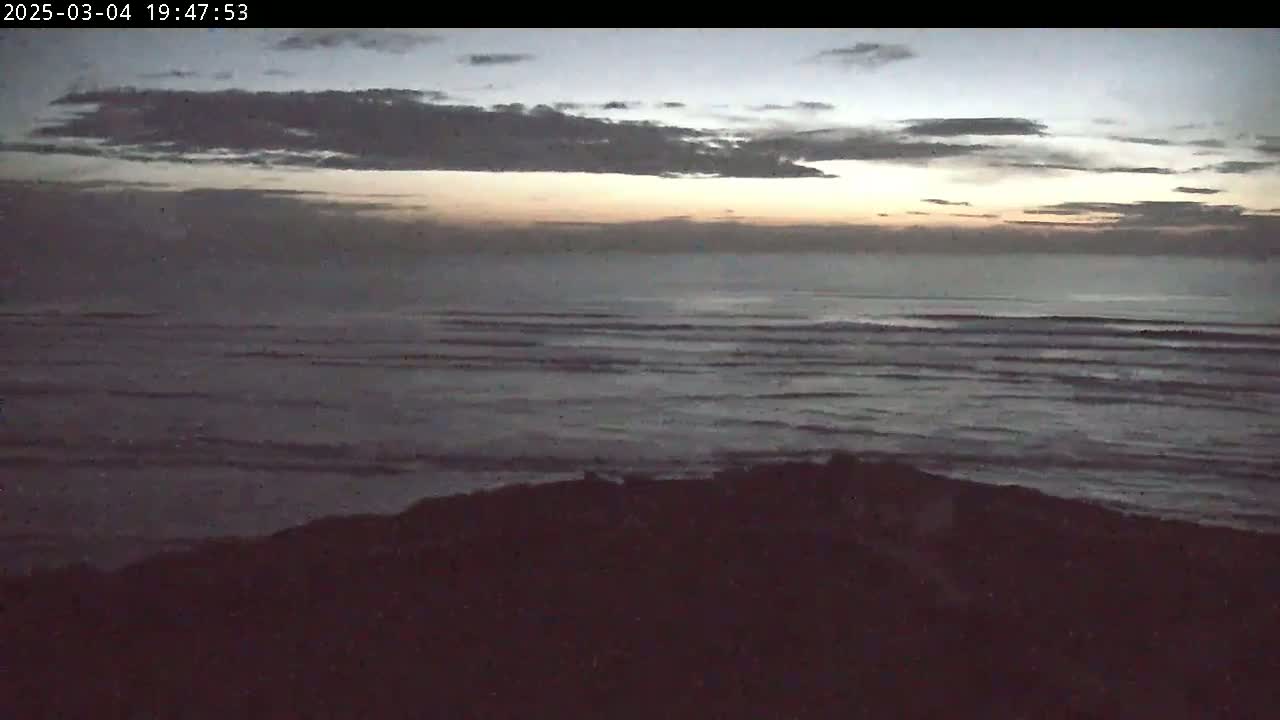 A dark, overcast sky with a hint of sunset colors over a calm ocean meeting a dark shoreline.