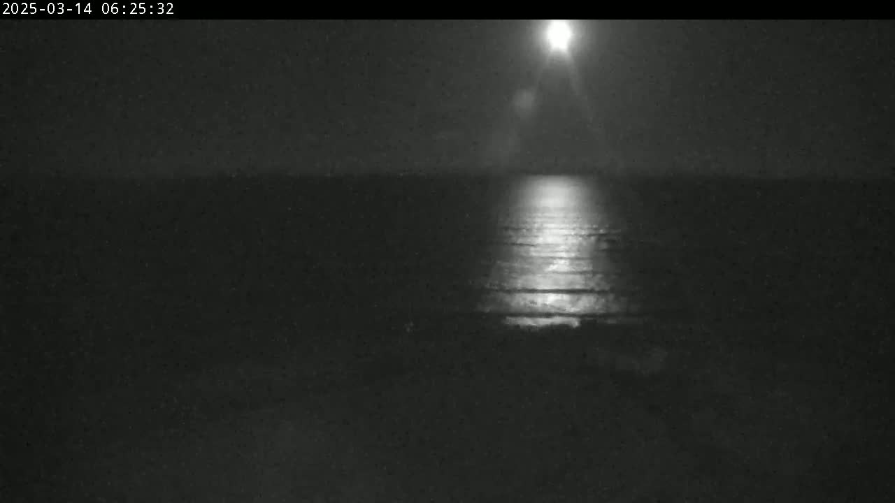 A bright moon shines on a dark body of water at night.