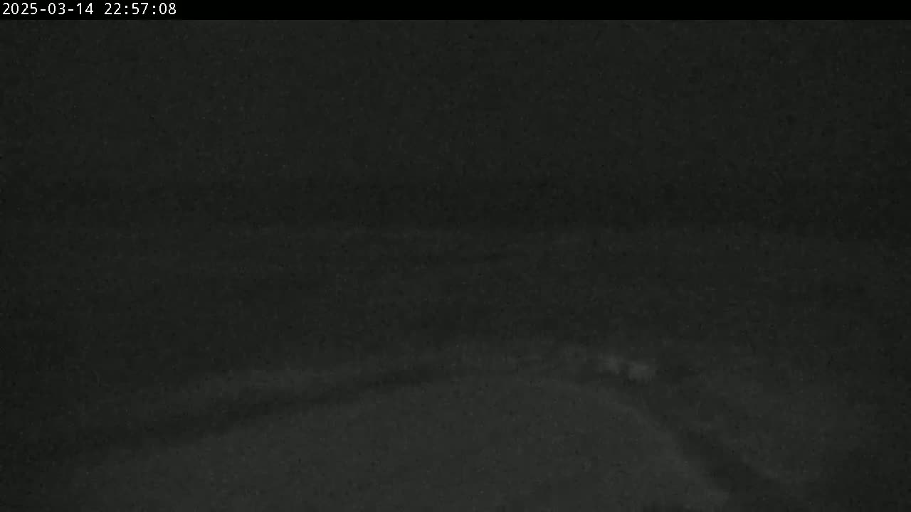 A dark, nighttime image shows a mostly indistinct landscape with a slightly lighter area possibly indicating a road or body of water.