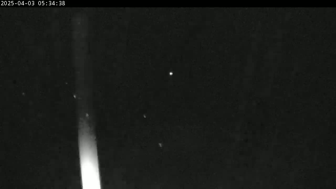 A bright vertical light streaks across a dark, night sky speckled with faint points of light.