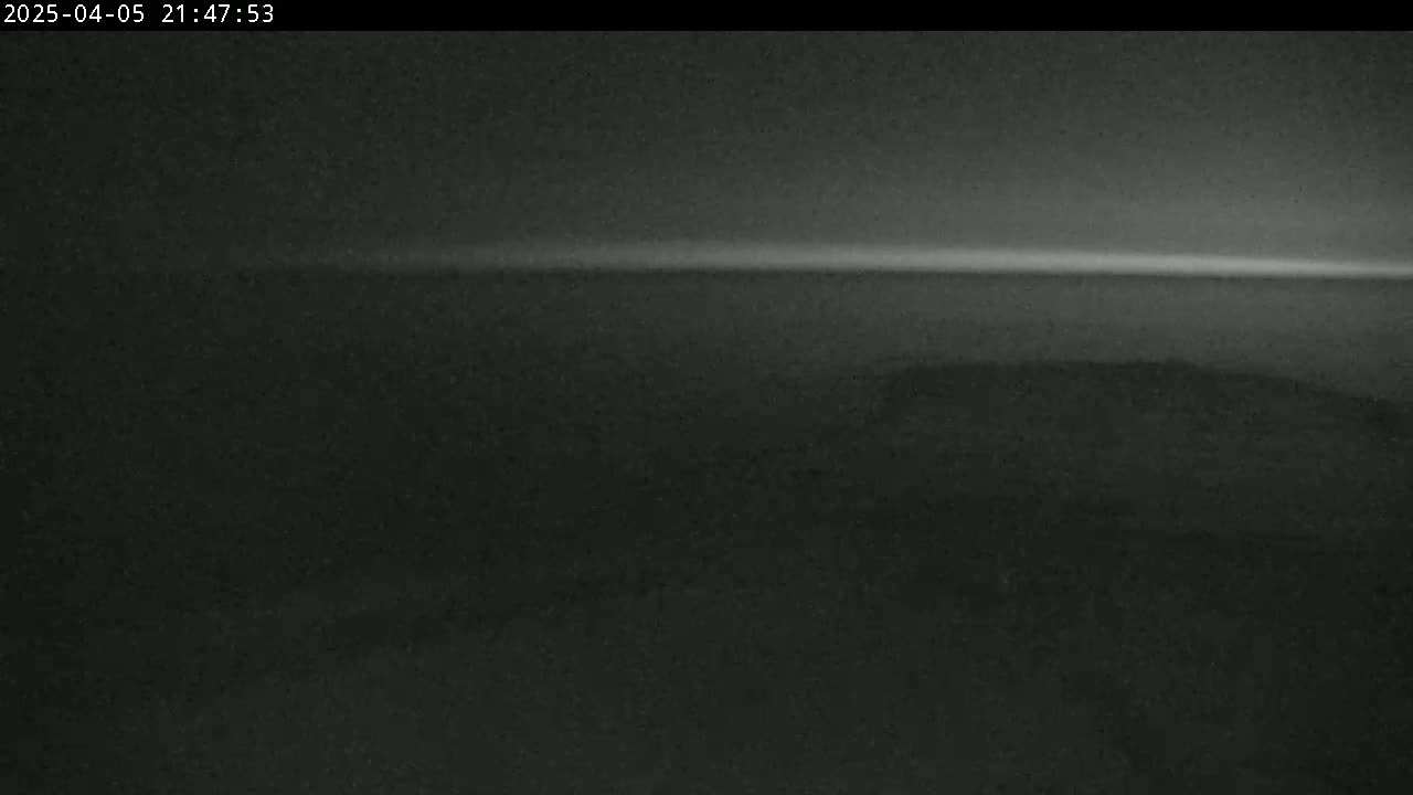 A low-light, nighttime view shows a dark landscape with a faintly brighter horizon line.
