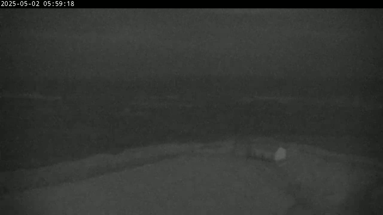 A low-light, nighttime image shows a dark, mostly featureless landscape with a small, indistinct structure near the bottom.